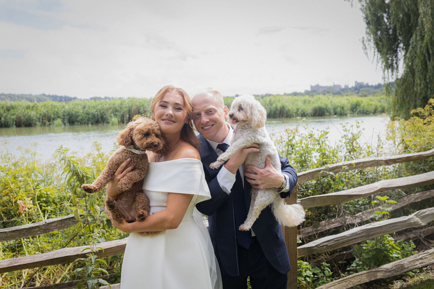 A loving couple shares tender moments along a rustic wooden fence overlooking a scenic lake and countryside.