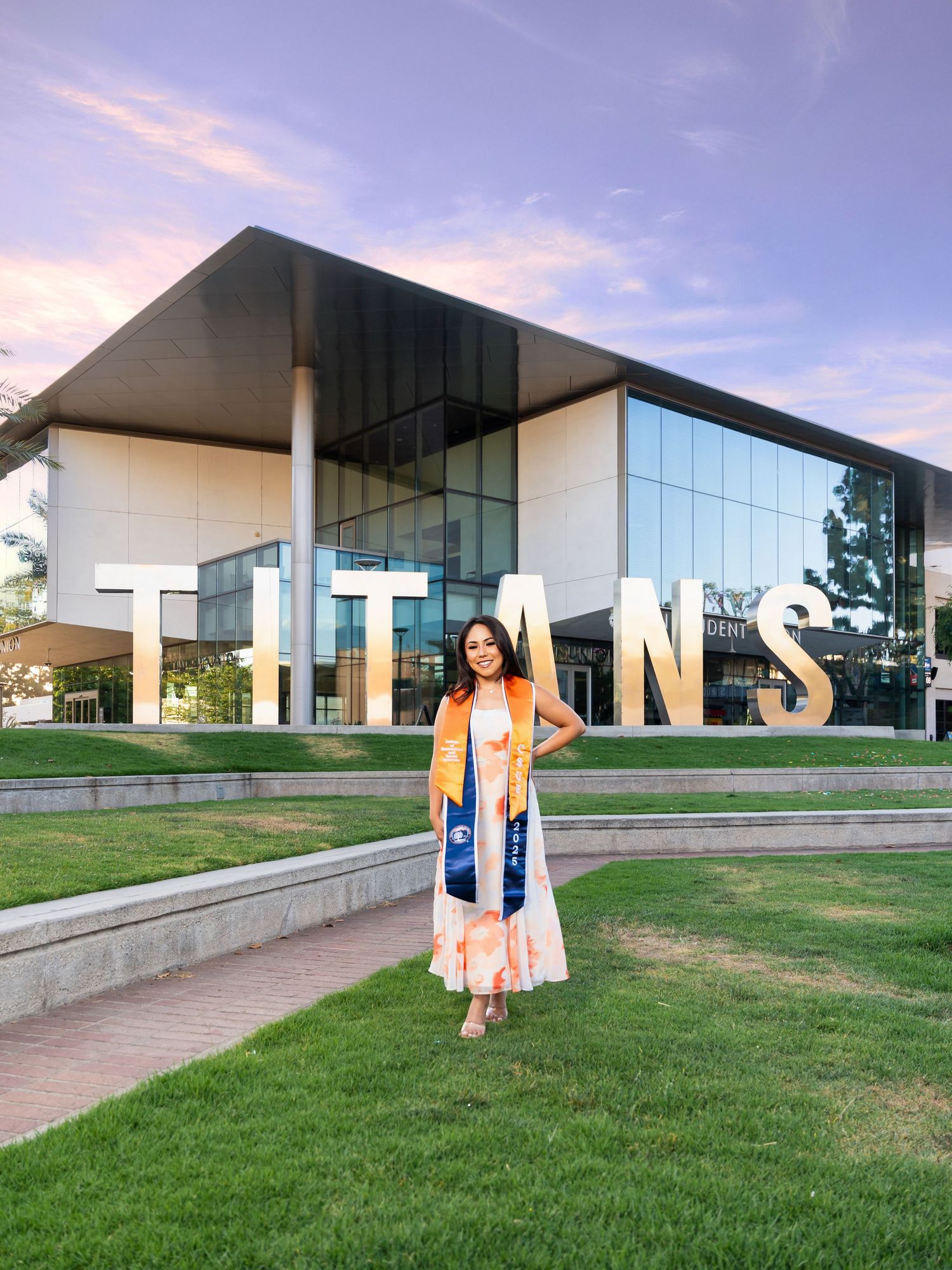 Modern architectural building with glass windows and sleek design sits on a grassy lawn during sunset.