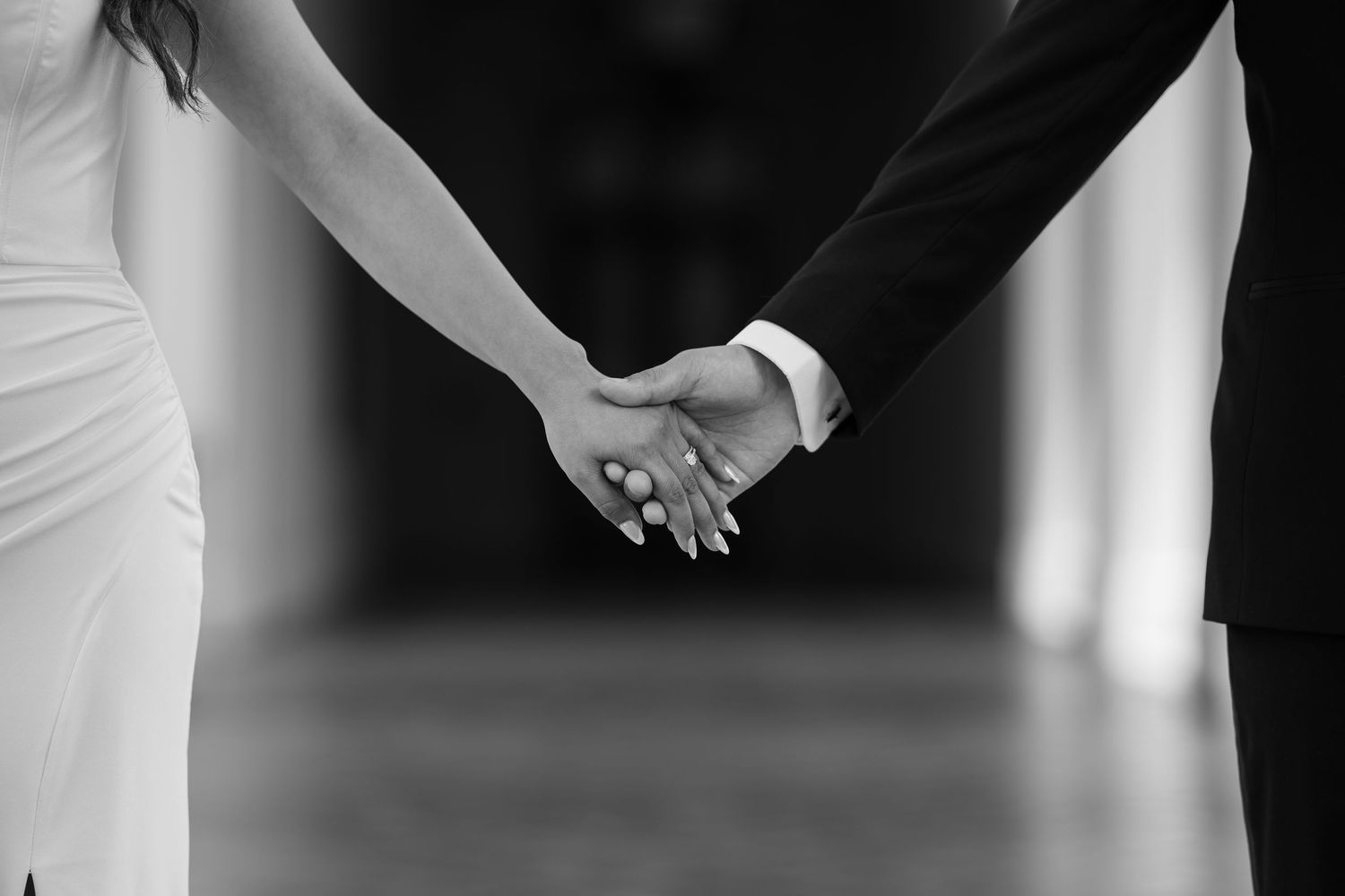 Black and white close-up of a couple holding hands showing wedding attire details.