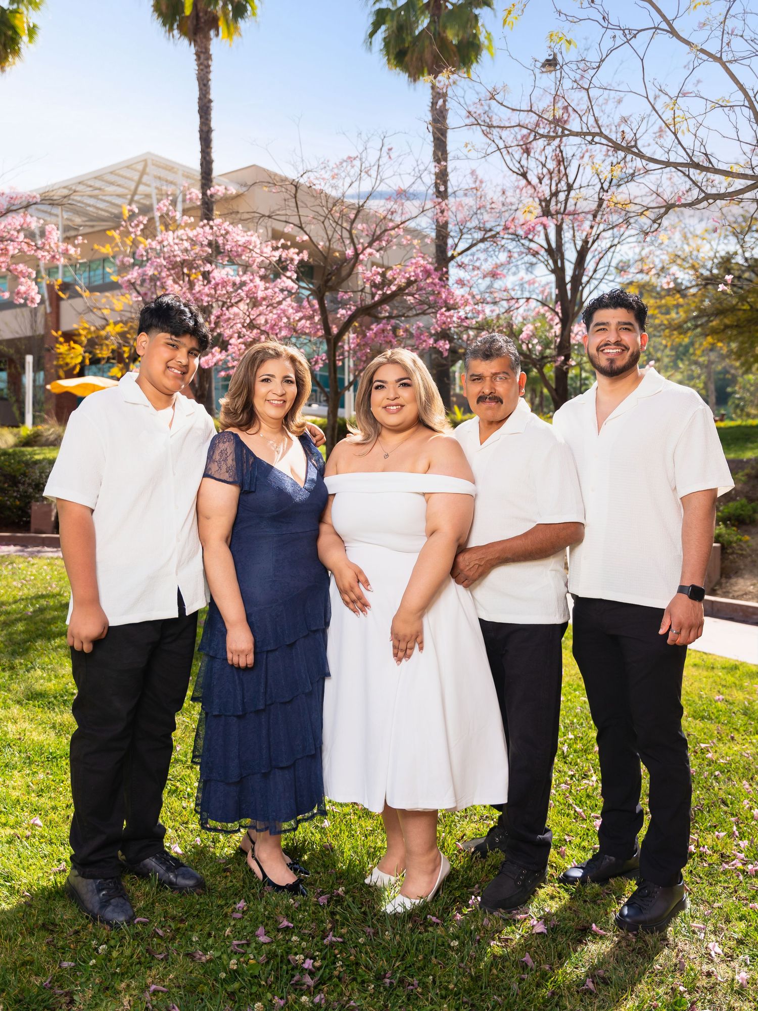 A group of people in coordinated navy and white outfits pose together in front of blooming cherry blossom trees.