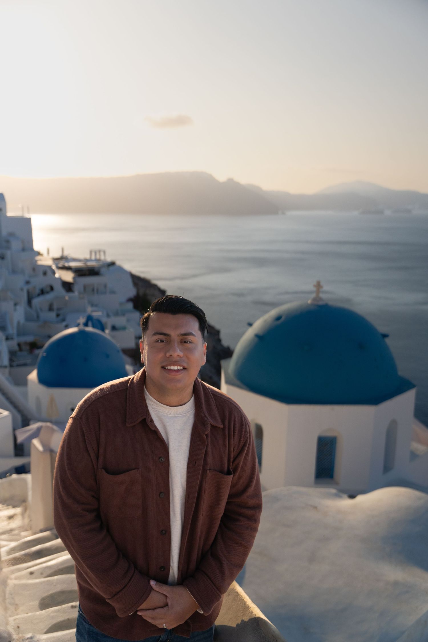 Scenic view of Santorini's iconic blue-domed churches and white buildings at sunset overlooking the Mediterranean Sea.