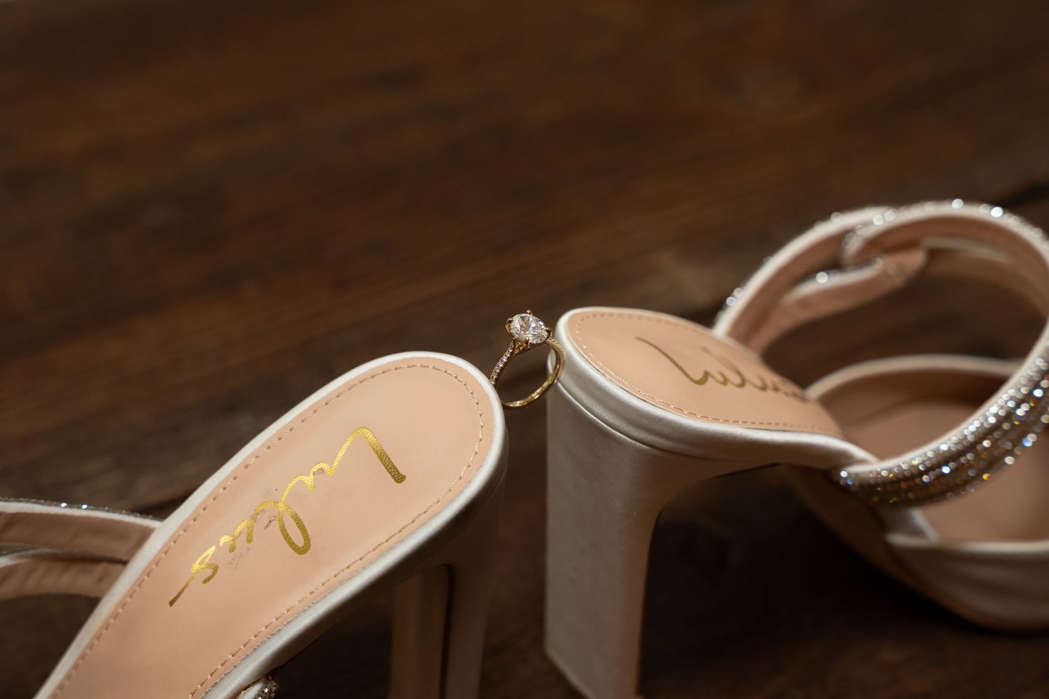 Elegant bridal shoes with delicate embellishments displayed on dark wooden background.
