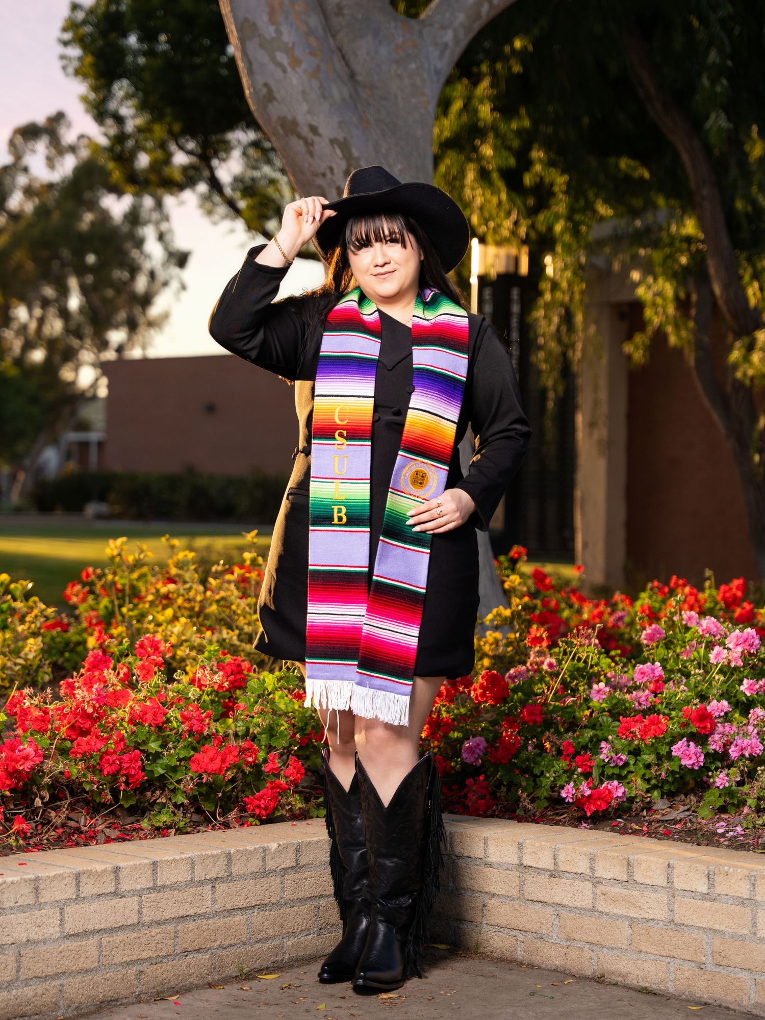 Colorful striped knit scarf displayed in autumn garden with blooming red roses and brick wall backdrop.
