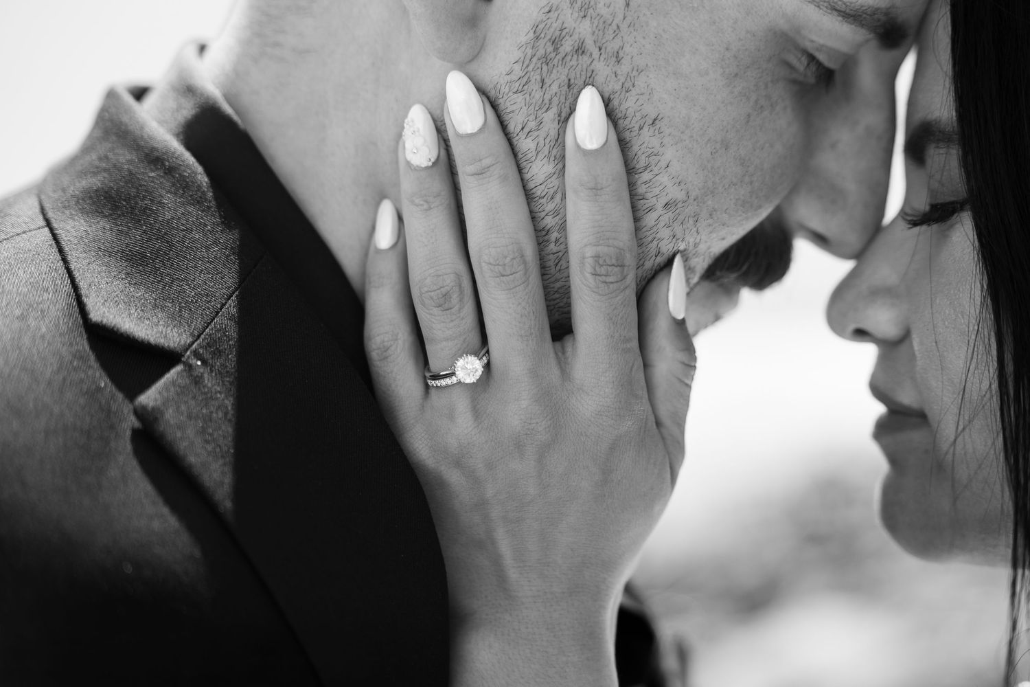 Intimate black and white portrait showing couple's tender moment with engagement ring visible.