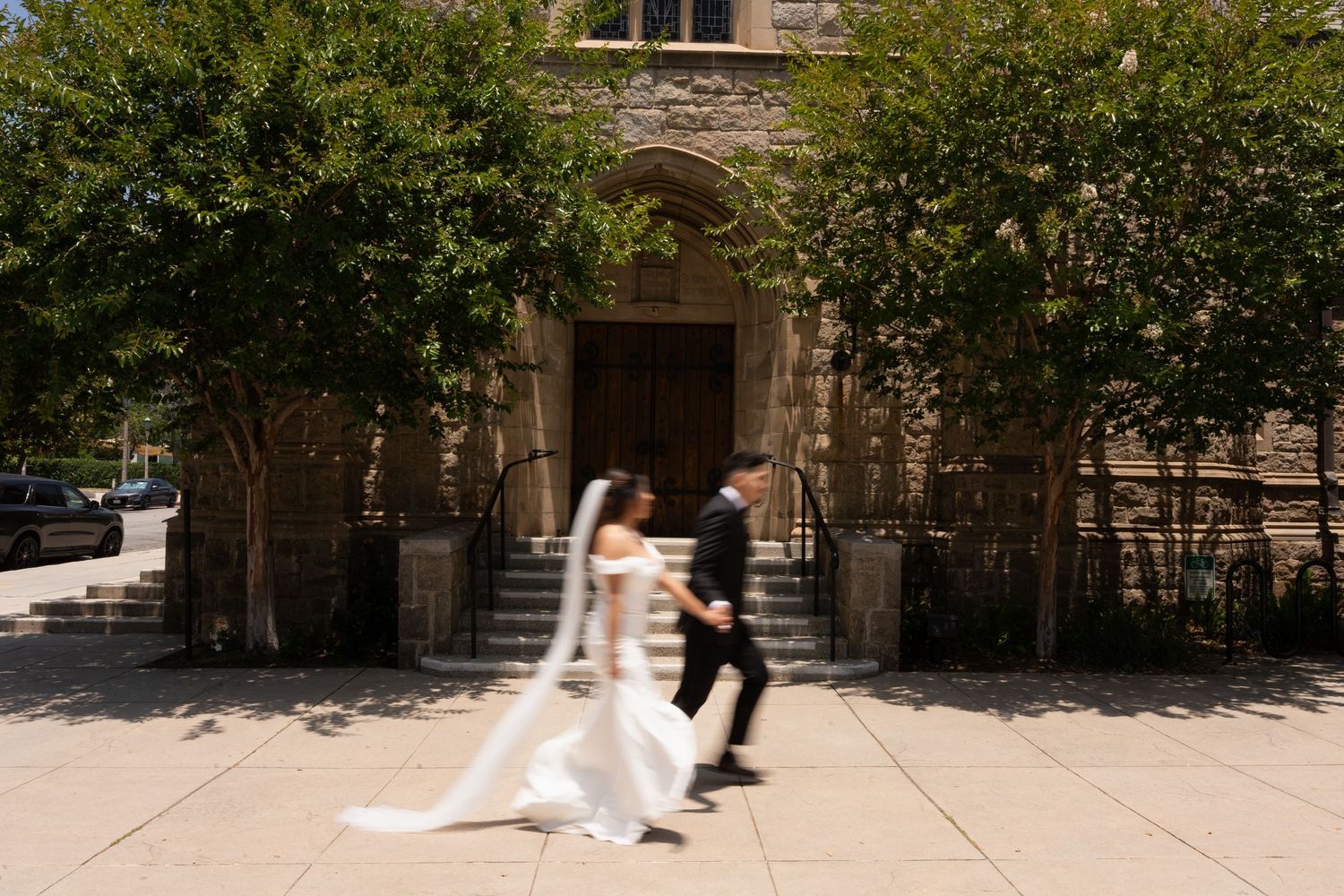 A wedding couple walking together along a scenic outdoor pathway with greenery and architecture.