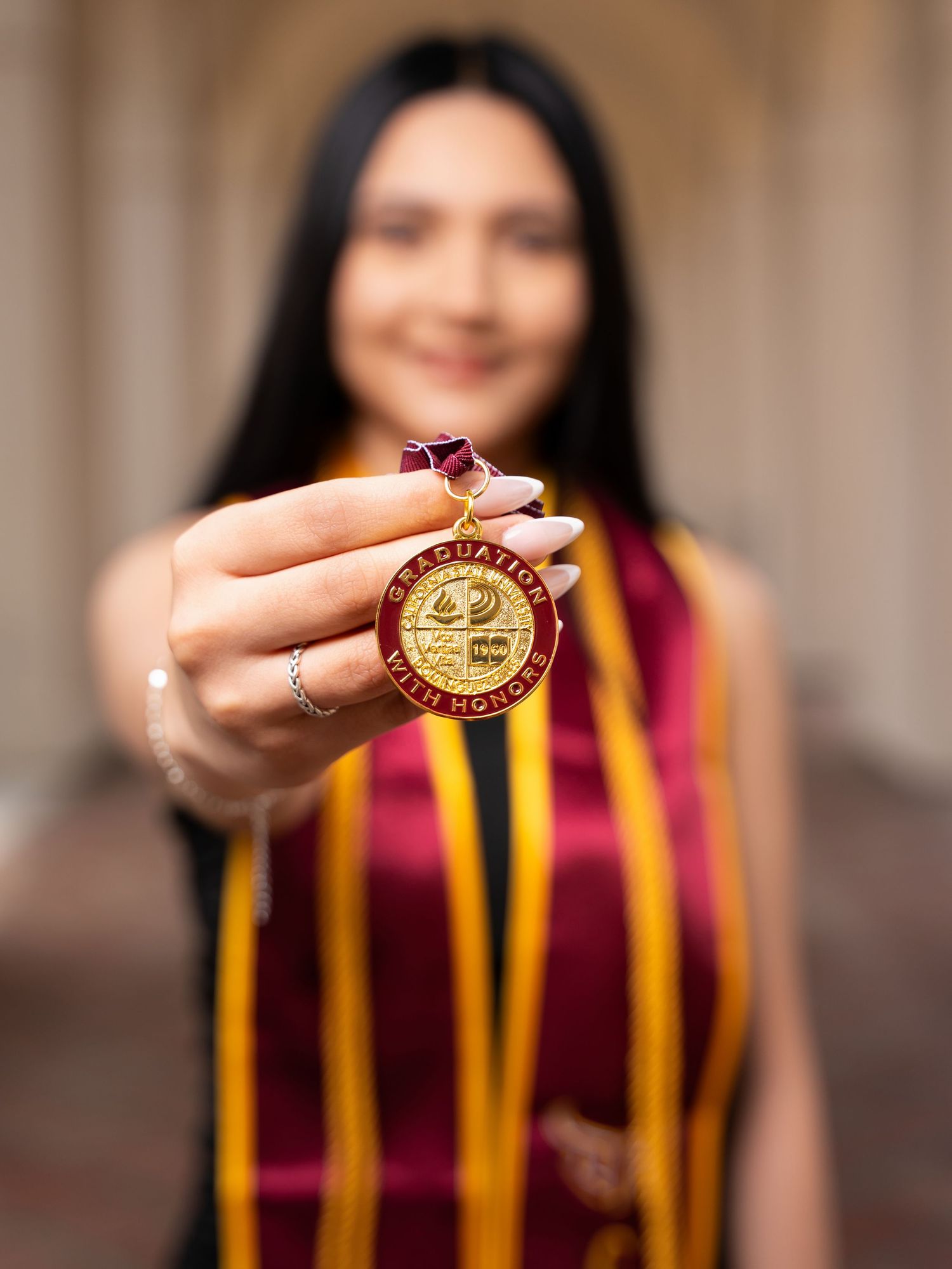 Person in maroon and yellow striped outfit holds up and displays a gold medallion or award.