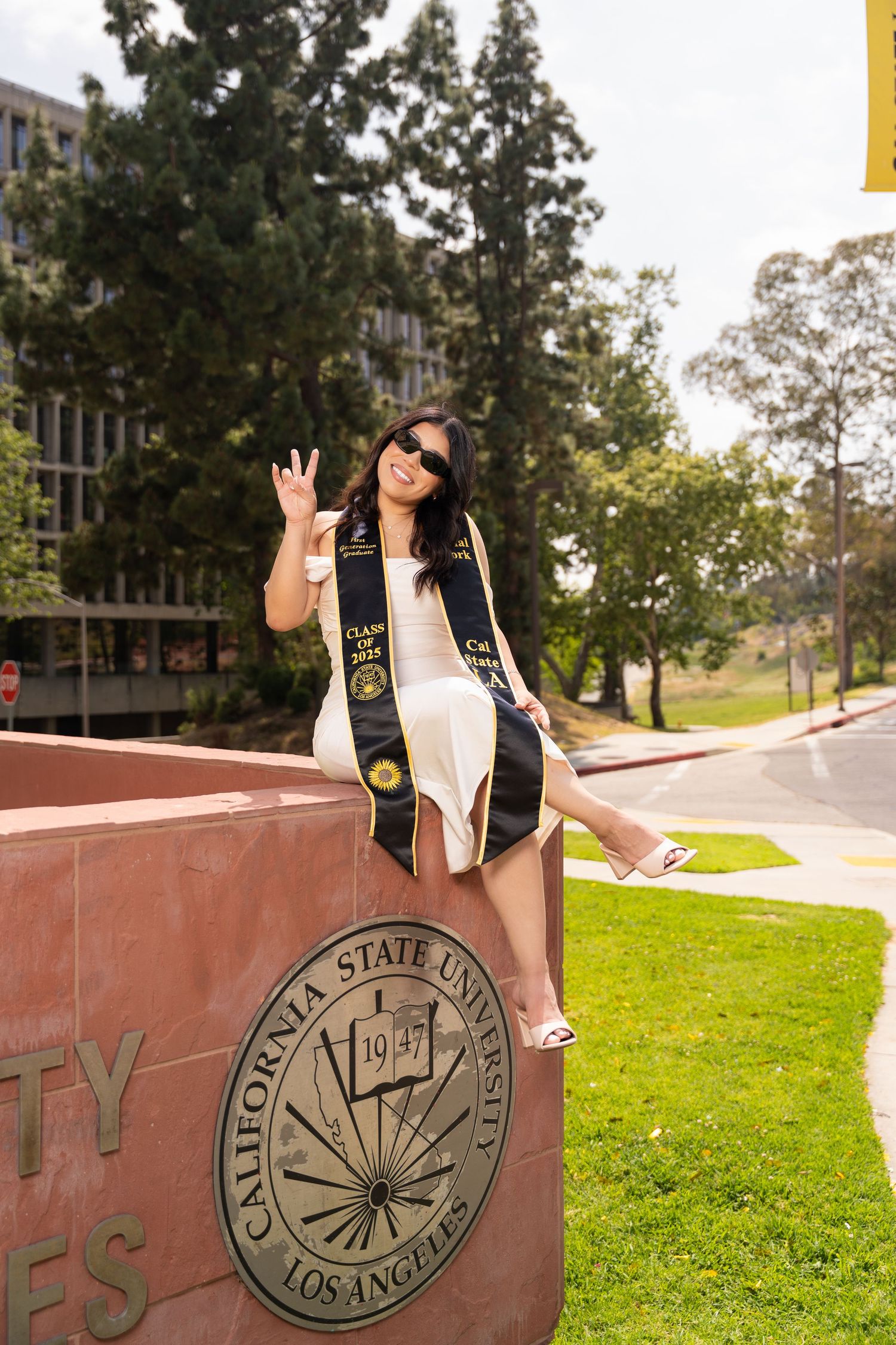 A graduate poses for a series of celebratory photos on a university campus with a large seal visible in the background.