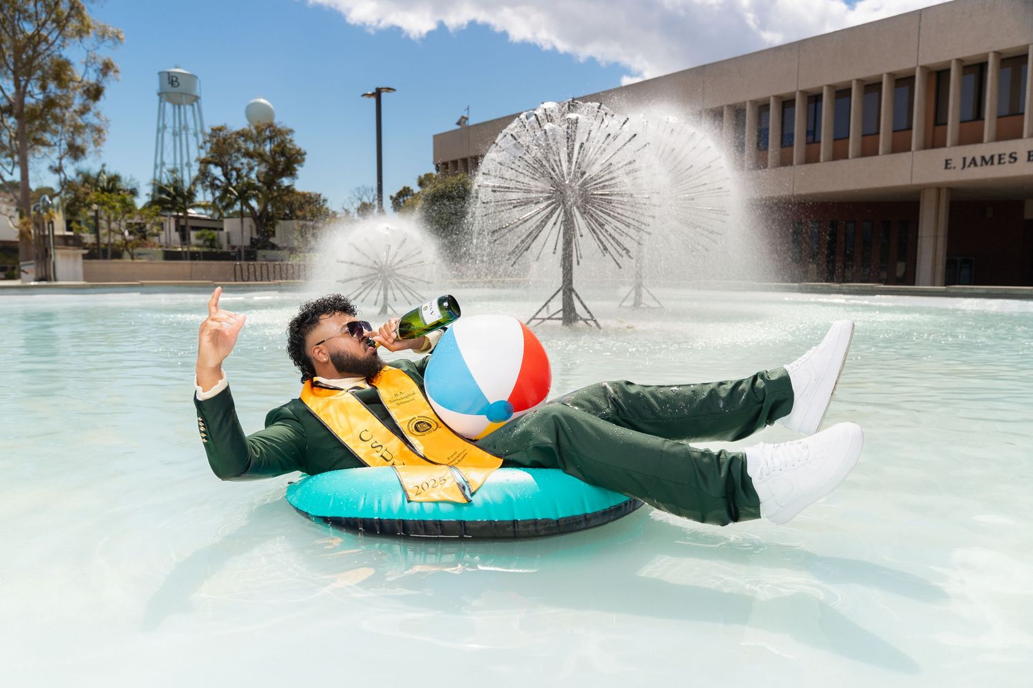 People enjoy tubing and splashing in a large outdoor water fountain pool on a sunny summer day.