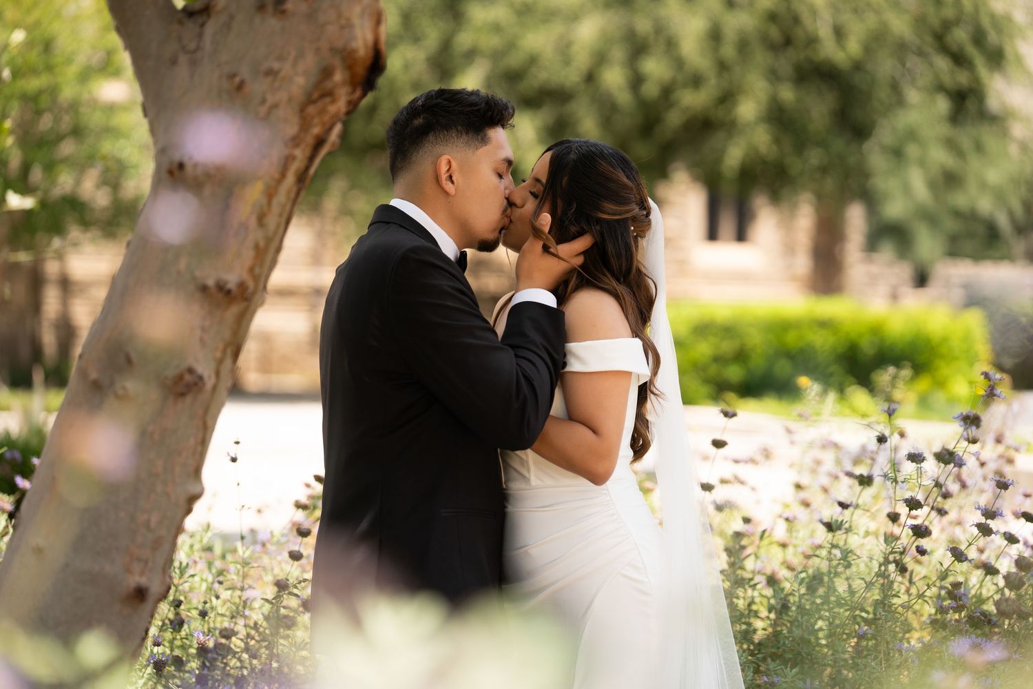 A romantic wedding moment in a garden setting with blooming white flowers and sunlit trees.