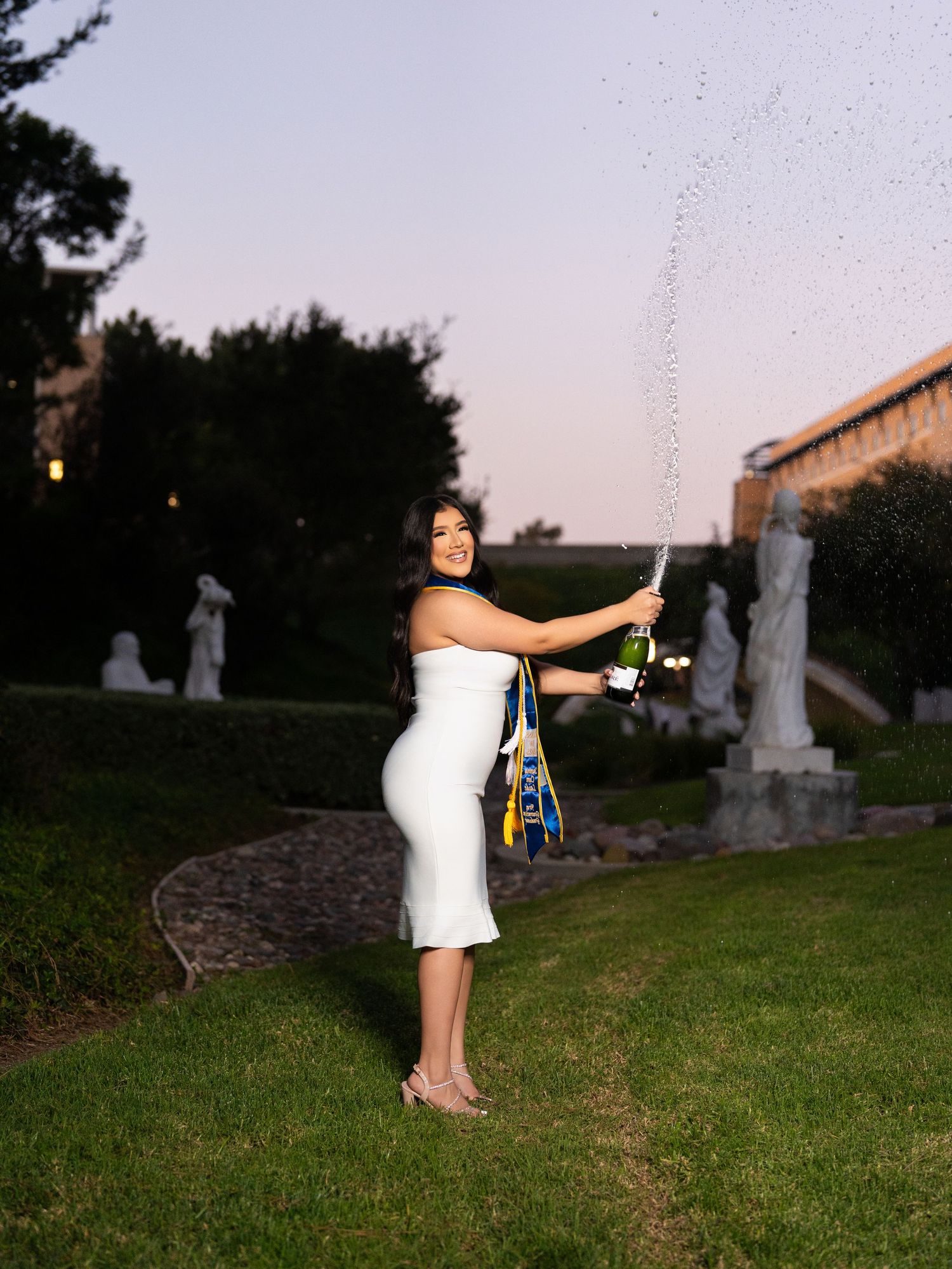 A person in a white dress poses playfully near gravestones in a cemetery at dusk.