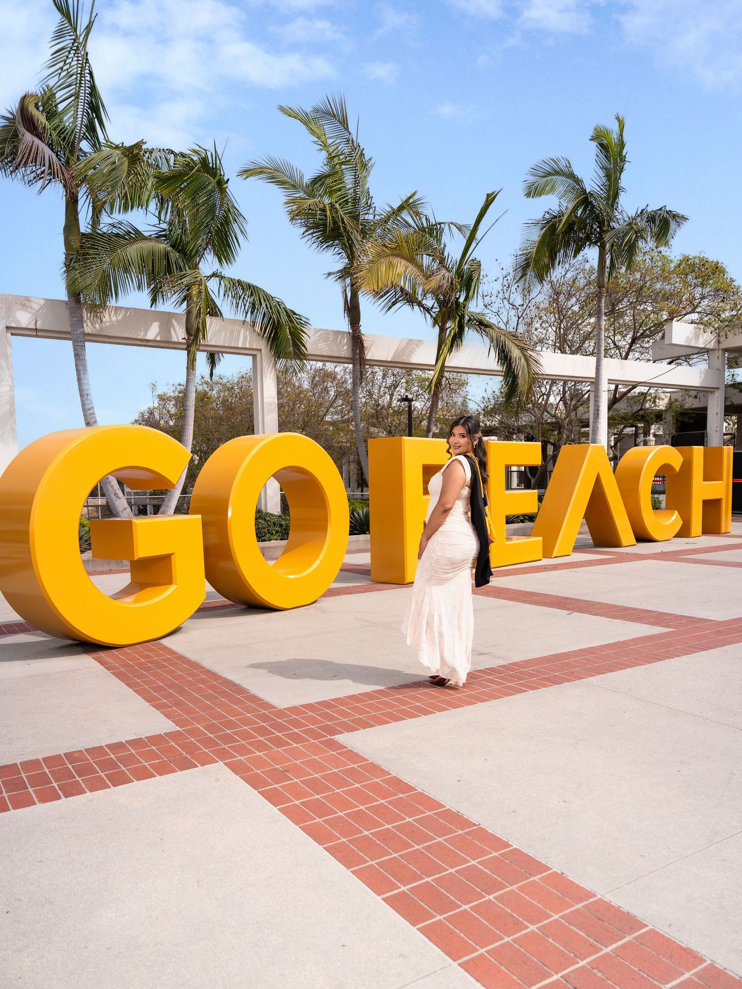 Woman posing in front of large yellow GO BEACH letters sign with palm trees at California State University Long Beach.