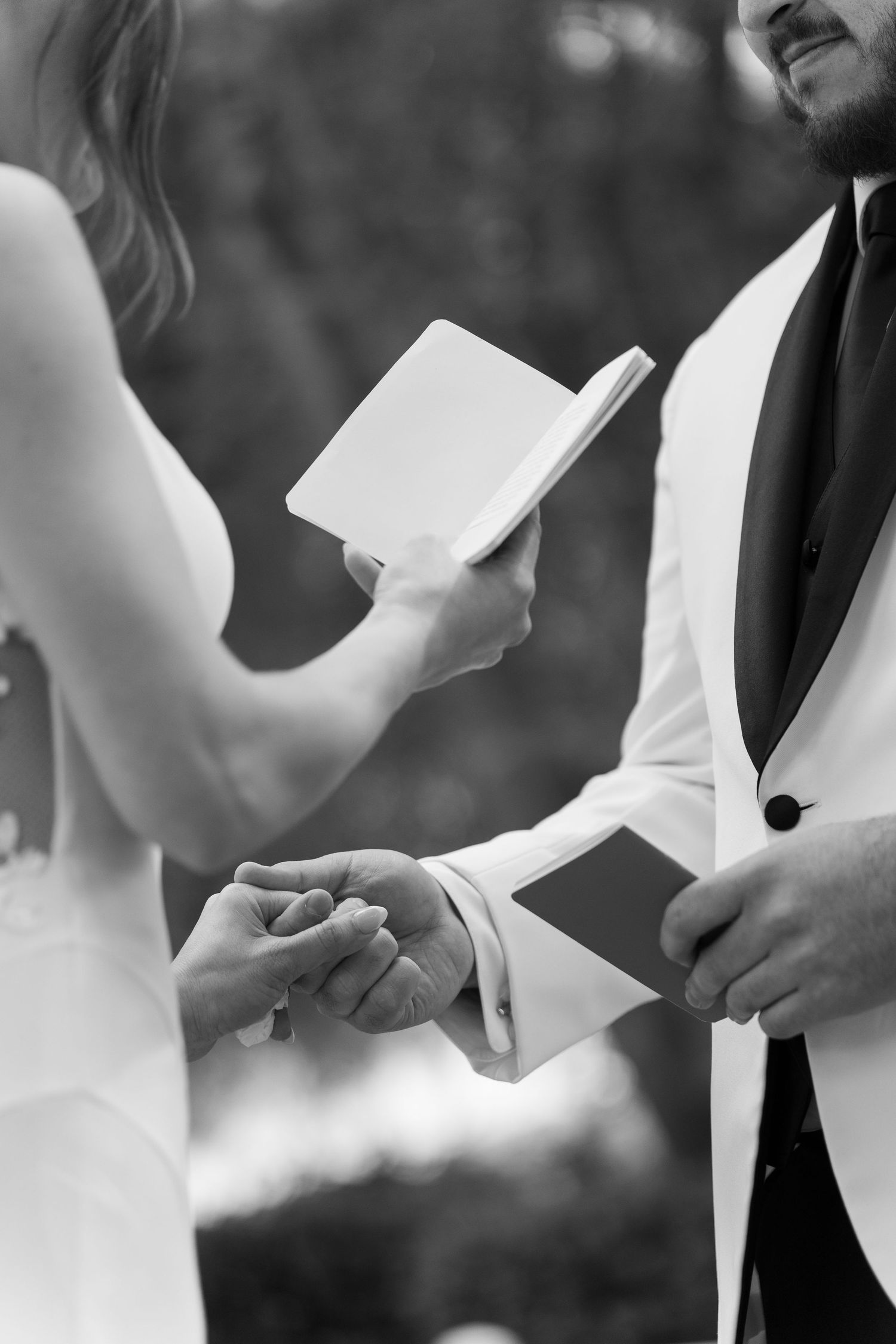 Wedding couple exchanging vows from white paper cards during outdoor ceremony.