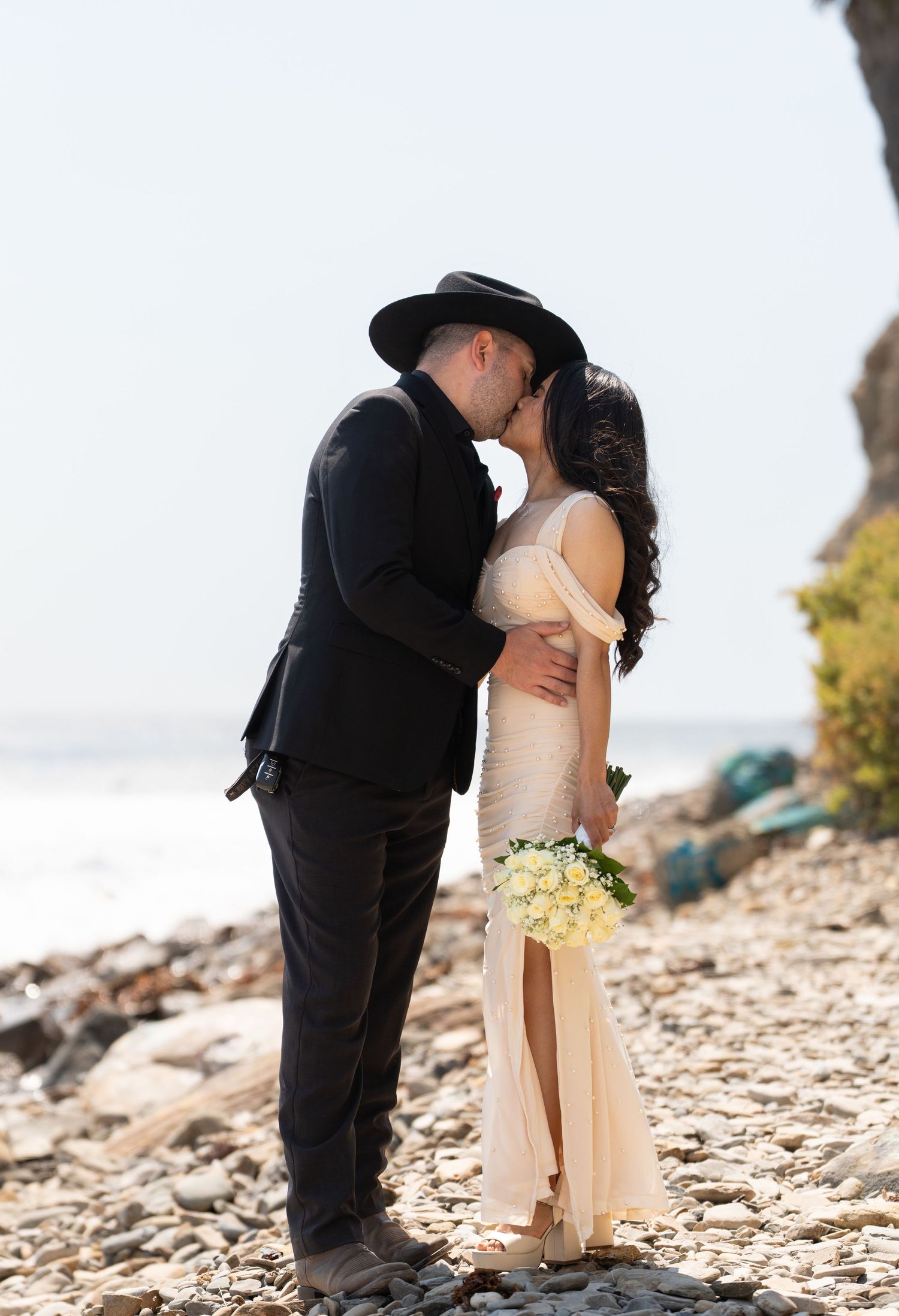 A romantic moment captured on a rocky beach with natural coastal scenery.