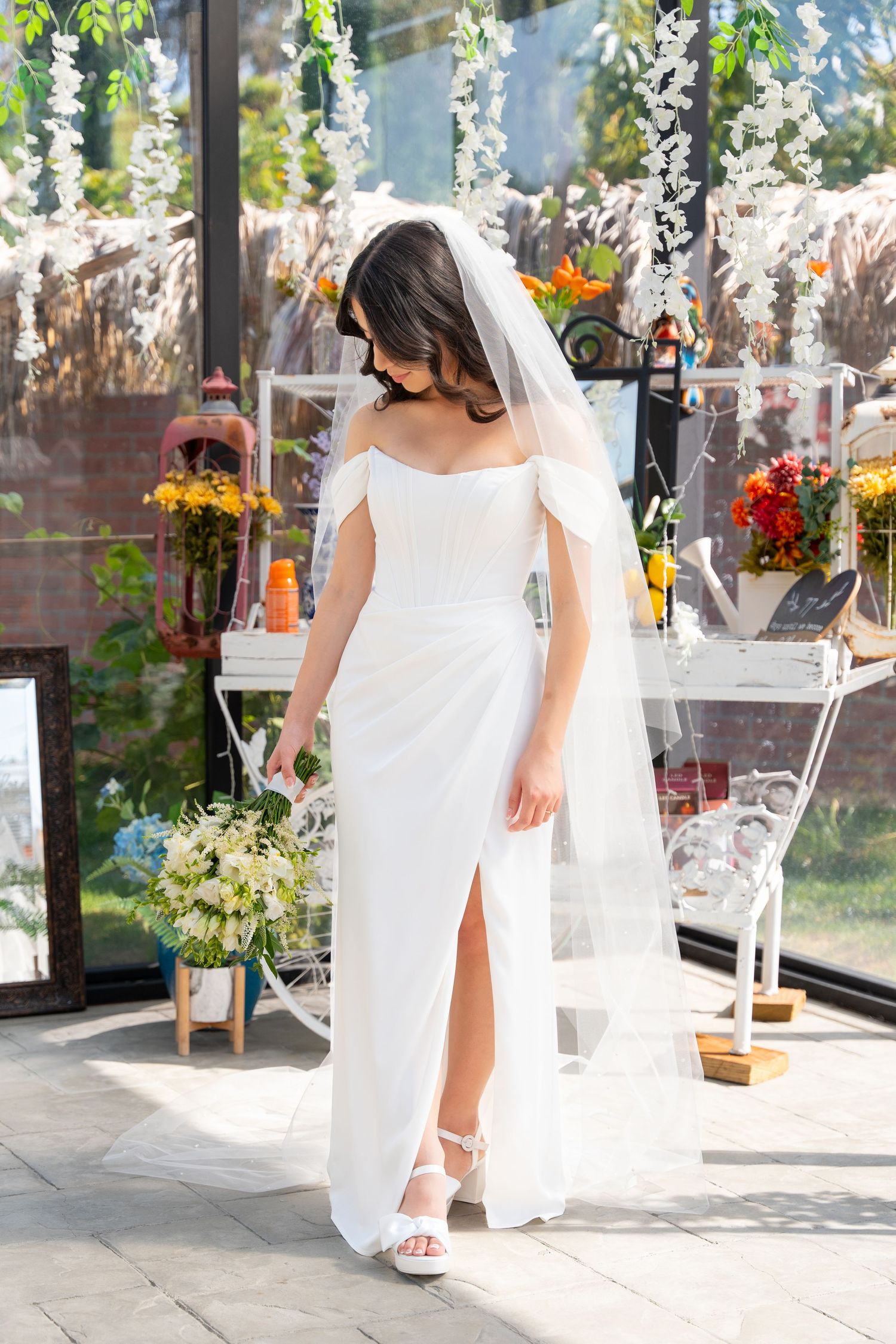 Elegant white wedding dress with slit photographed in greenhouse setting with hanging floral decor.