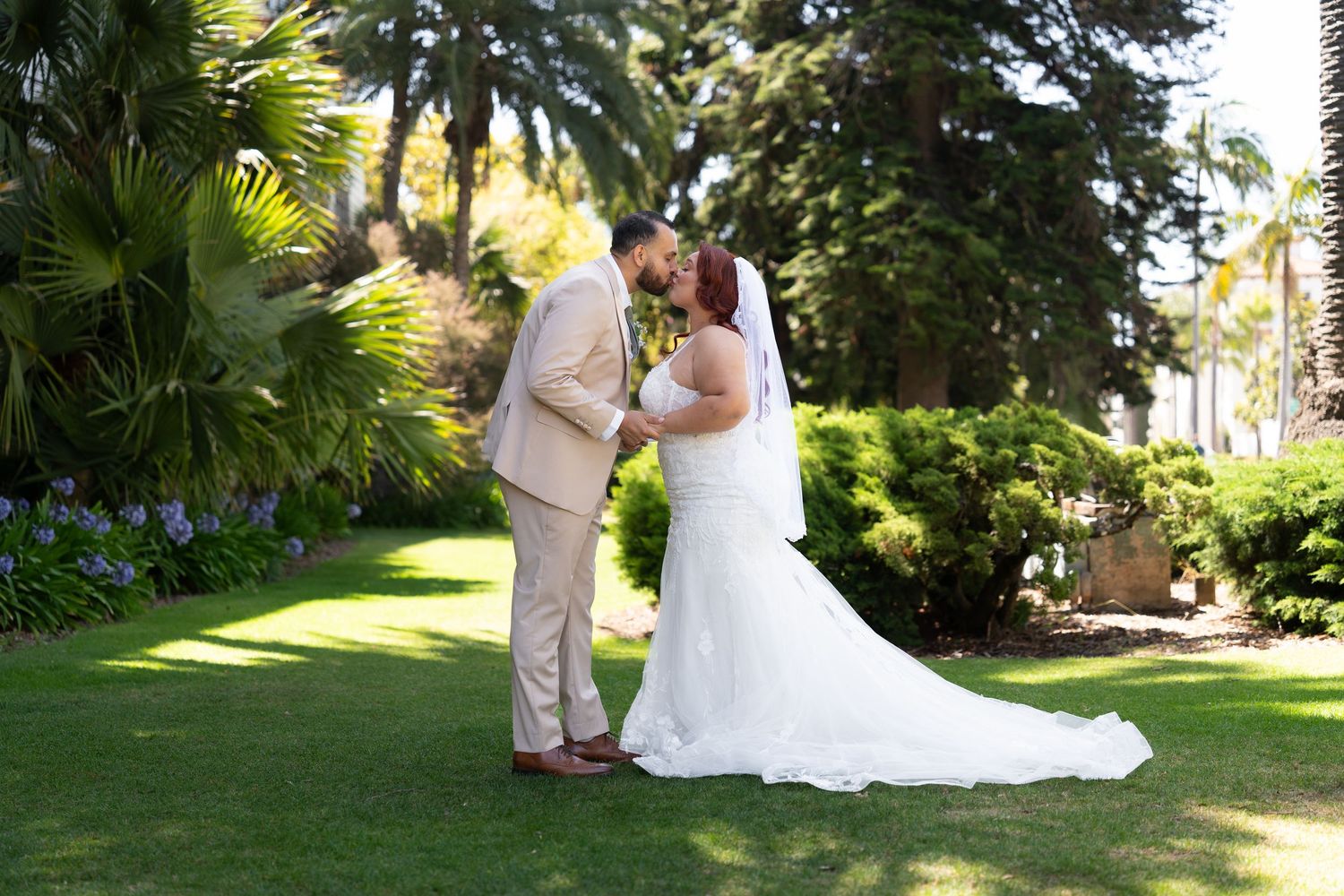 Romantic wedding couple poses in front of lush tropical garden setting at outdoor venue.