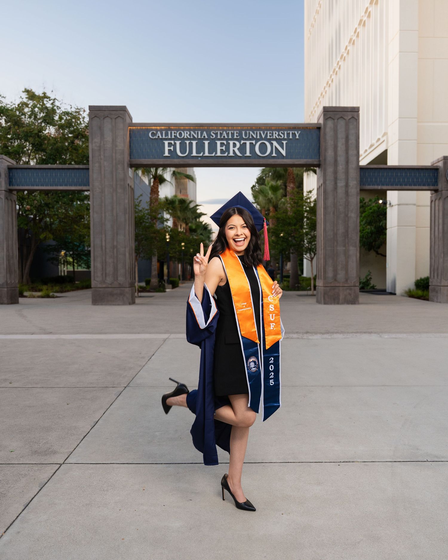 Graduate poses in front of California State University Fullerton entrance sign during commencement ceremony.