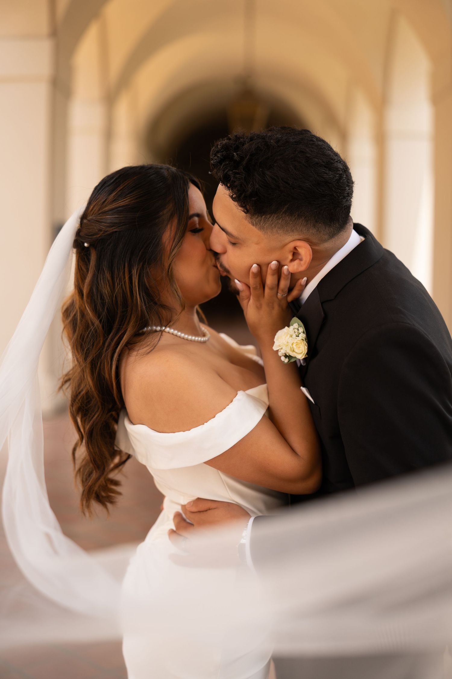 Romantic wedding couple embracing under arched colonnade with soft lighting.