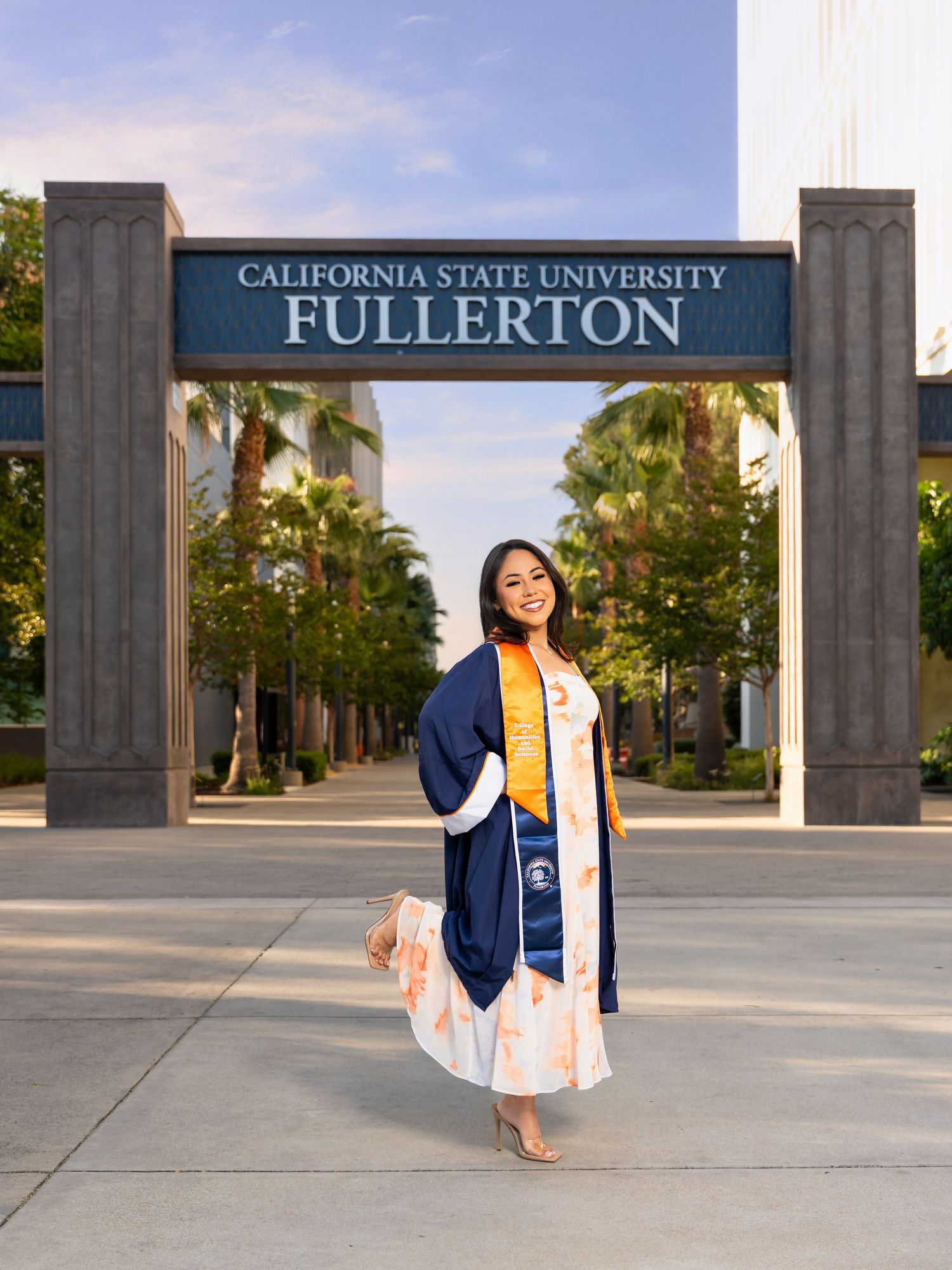A graduate in academic regalia poses for photos at California State University Fullerton's entrance sign.