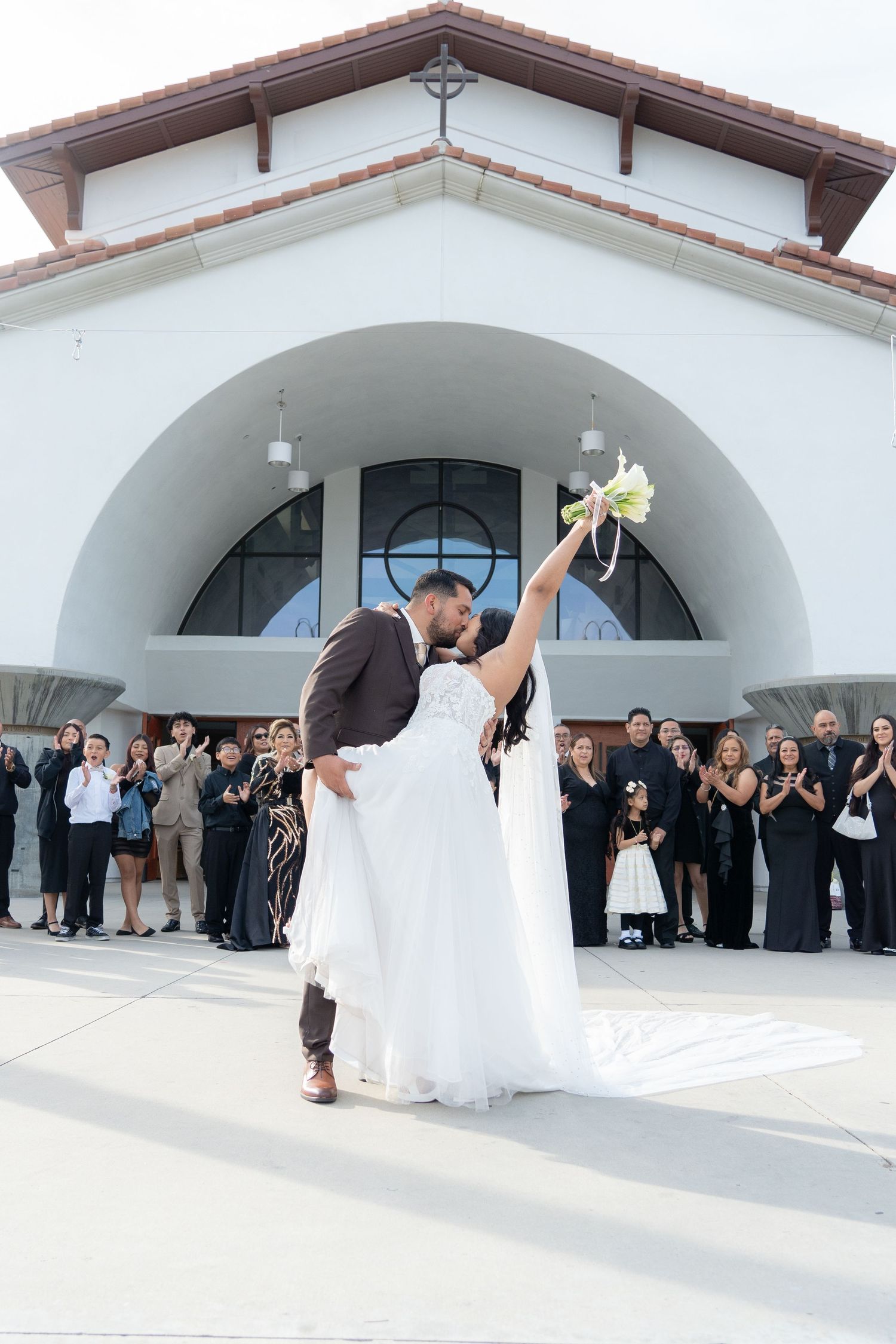 A bride and groom share a romantic dip during their first dance outside an elegant white Spanish-style church building.