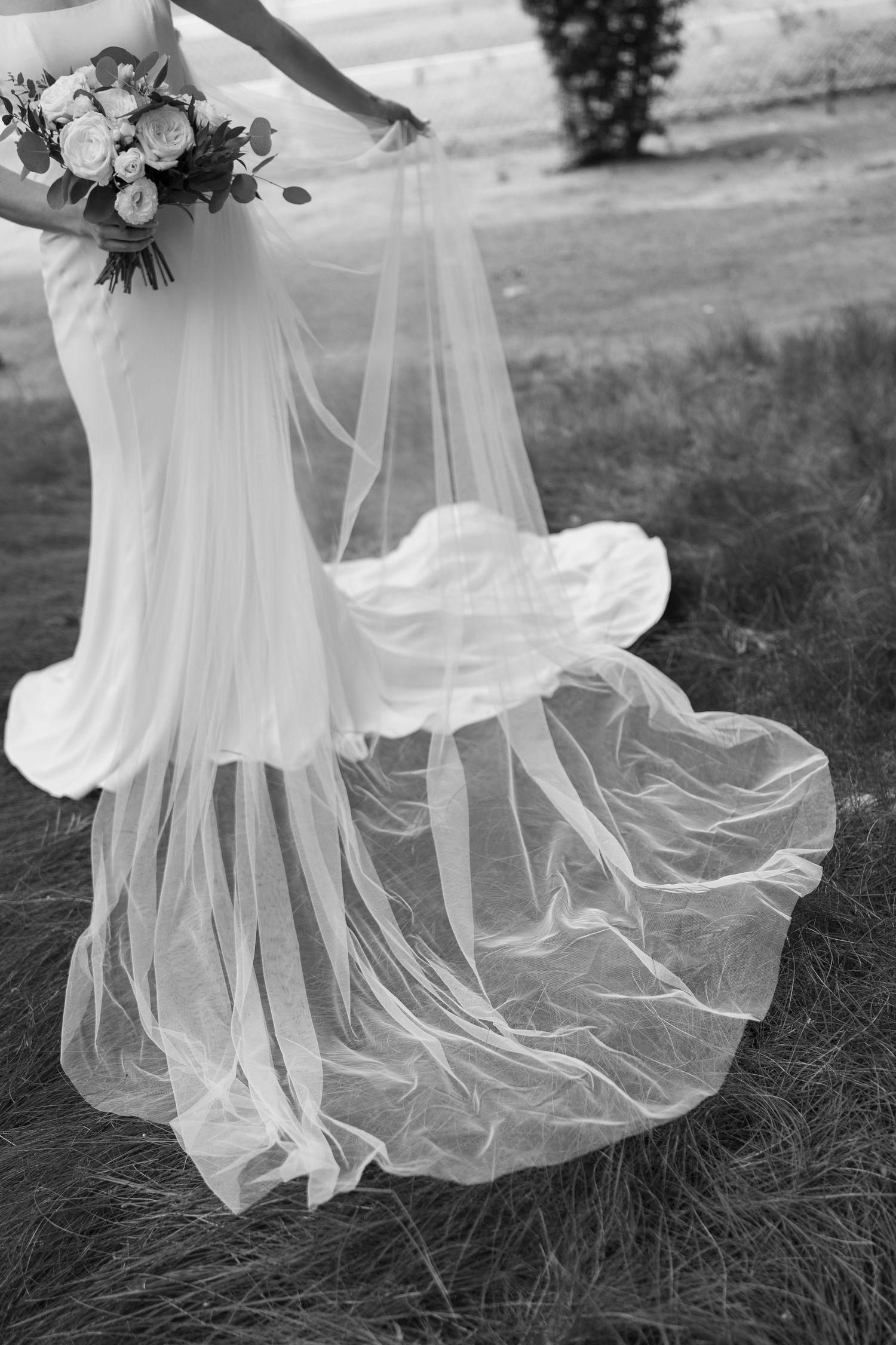 Black and white detail of a flowing wedding dress veil and bouquet.