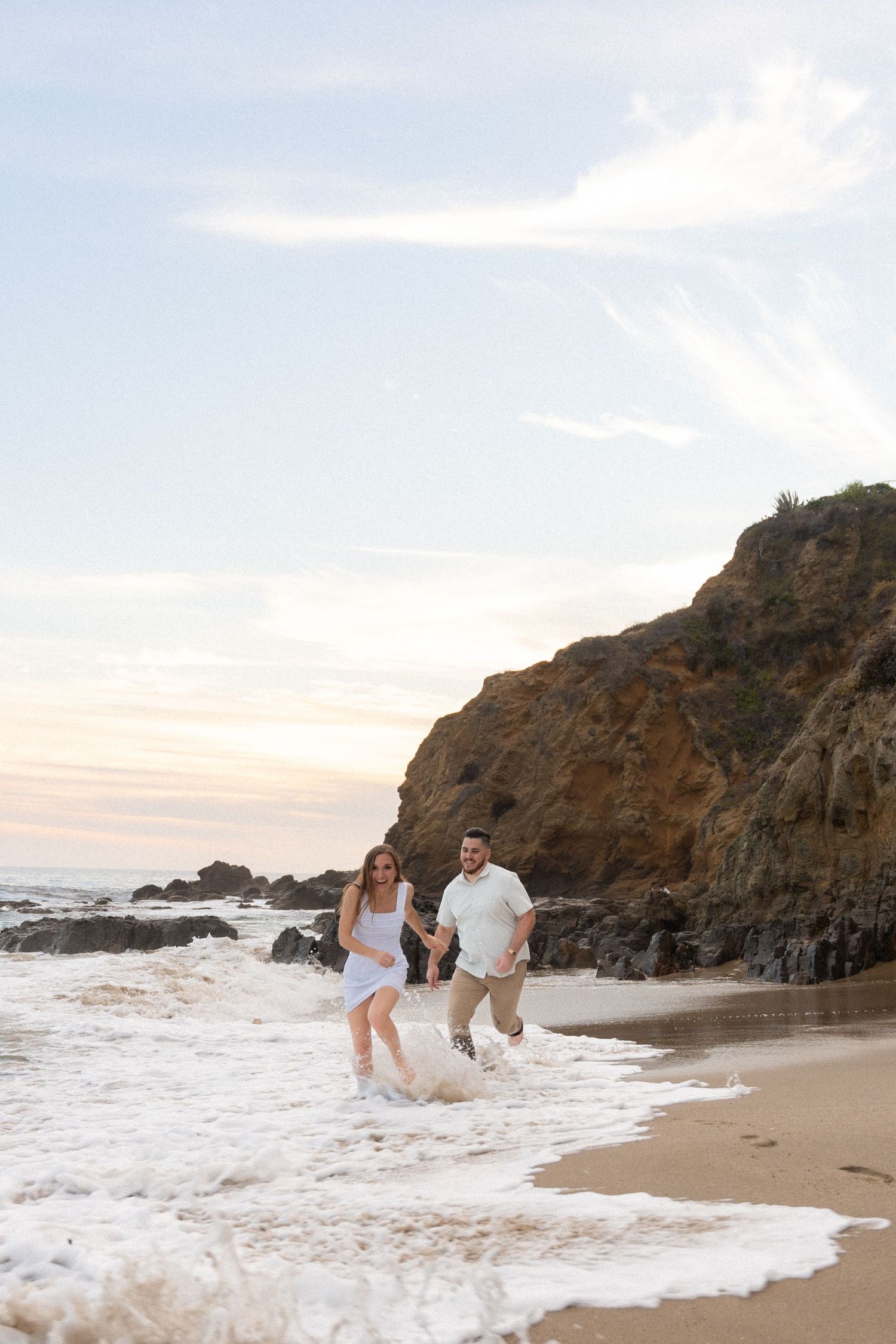 People walking together along a scenic rocky beach at sunset as ocean waves crash against the shore.