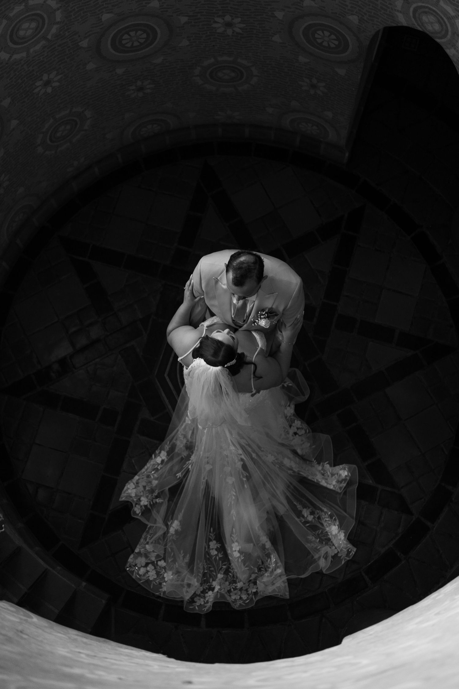 Dramatic overhead black and white shot of couple dancing on circular patterned floor.
