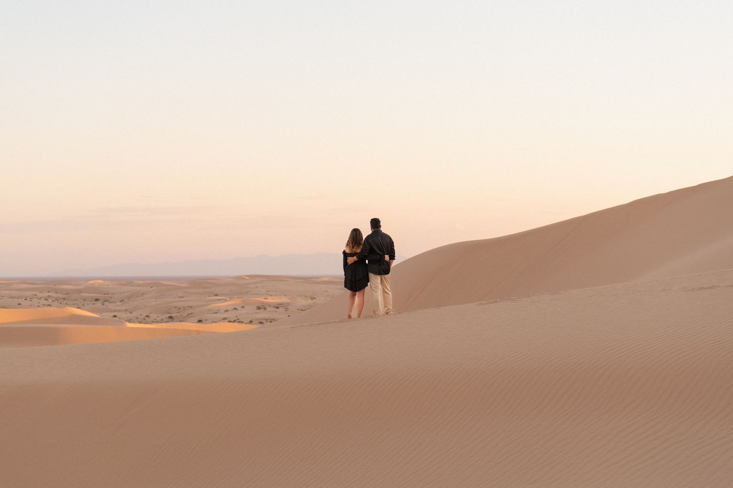 Silhouettes of people standing on sand dunes during sunset in a vast desert landscape.