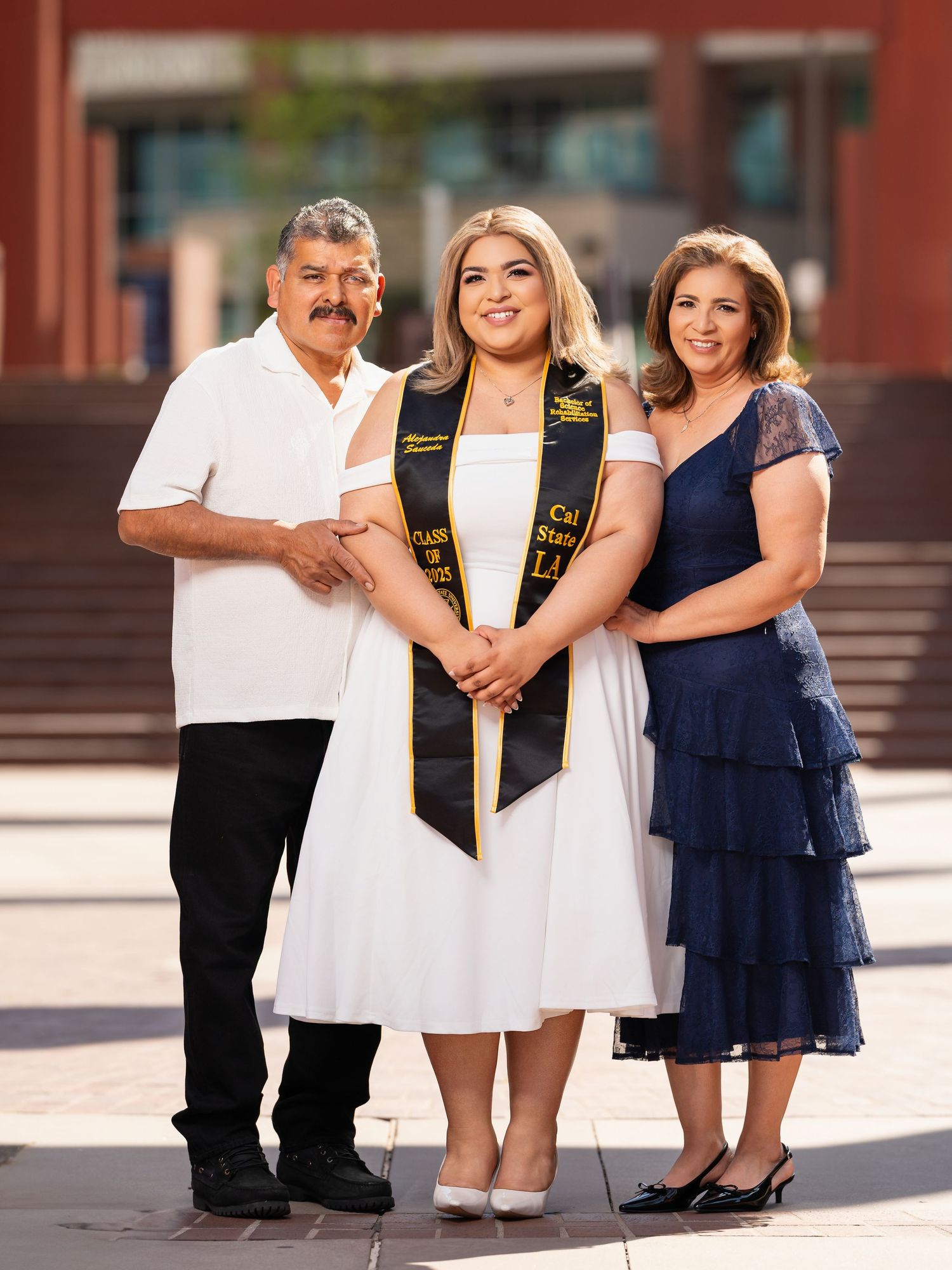 Family wearing coordinated white and navy outfits poses together for graduation photos outdoors.