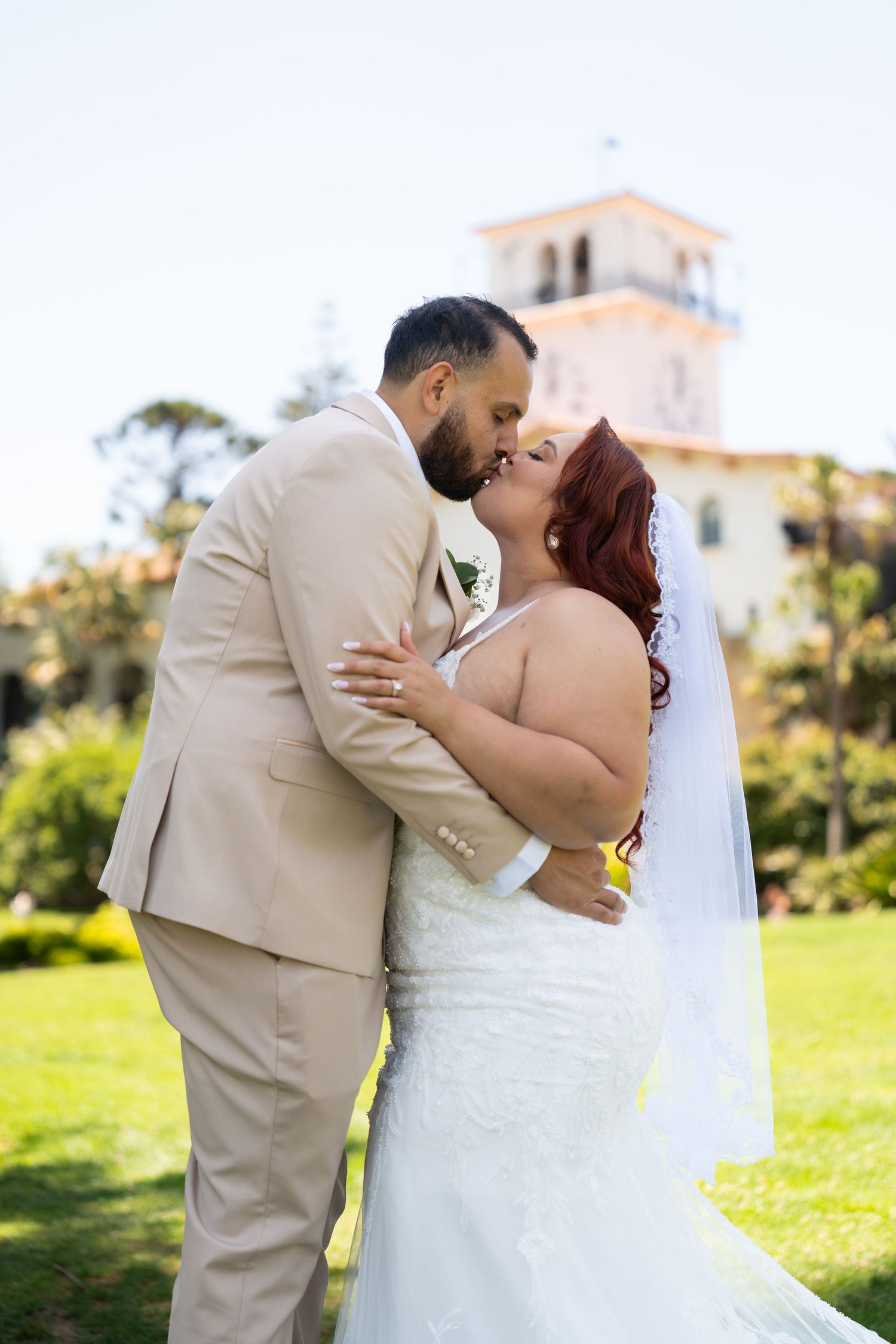 Romantic moment captured between newlyweds on sunny lawn with white church in background.