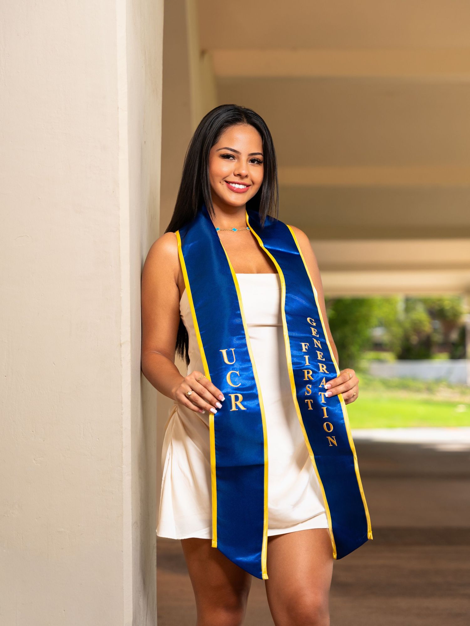 Graduate wearing a royal blue and yellow stole with white dress poses for graduation photos in an outdoor setting.