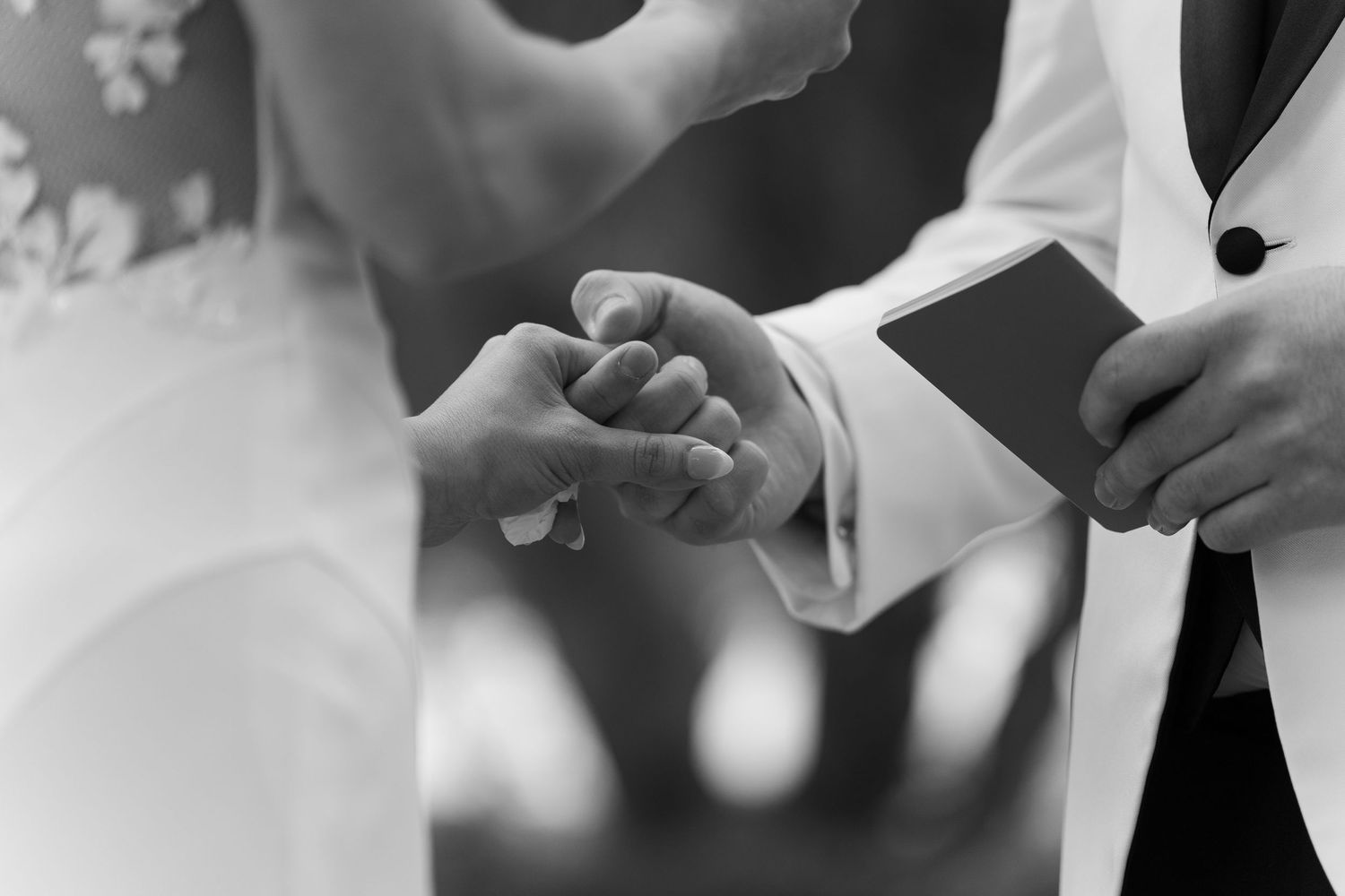 Black and white close-up photo of hands exchanging rings during a wedding ceremony.