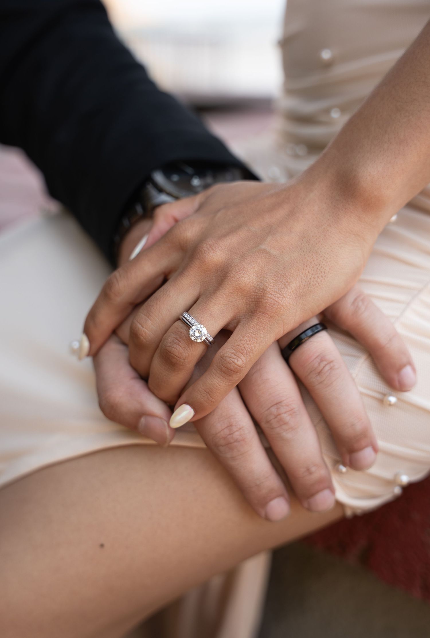 Close-up of intertwined hands showing wedding rings against a light-colored fabric.