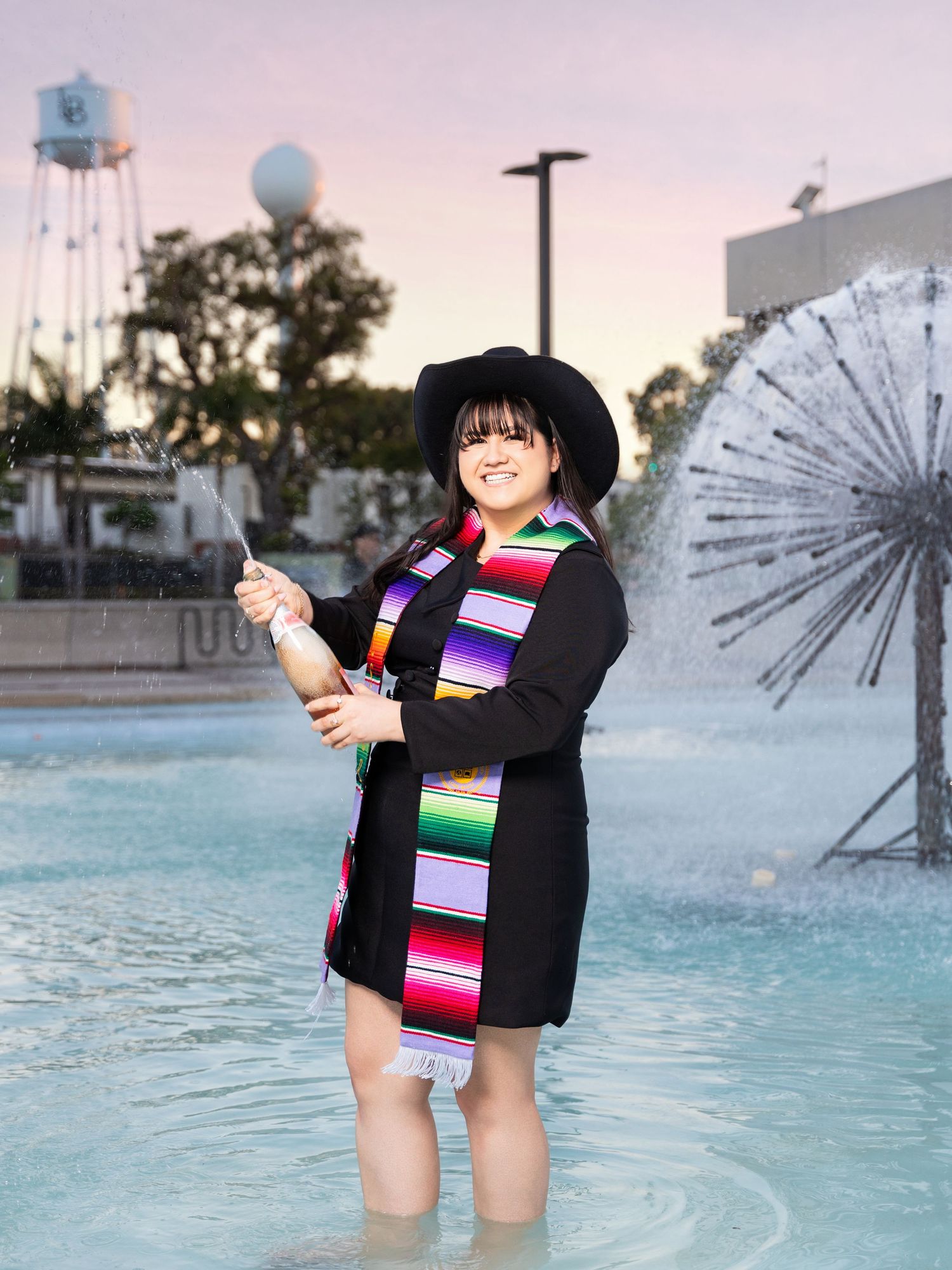 Four sequential photos show a person in a black outfit with a colorful serape-style sash posing by a fountain at sunset.