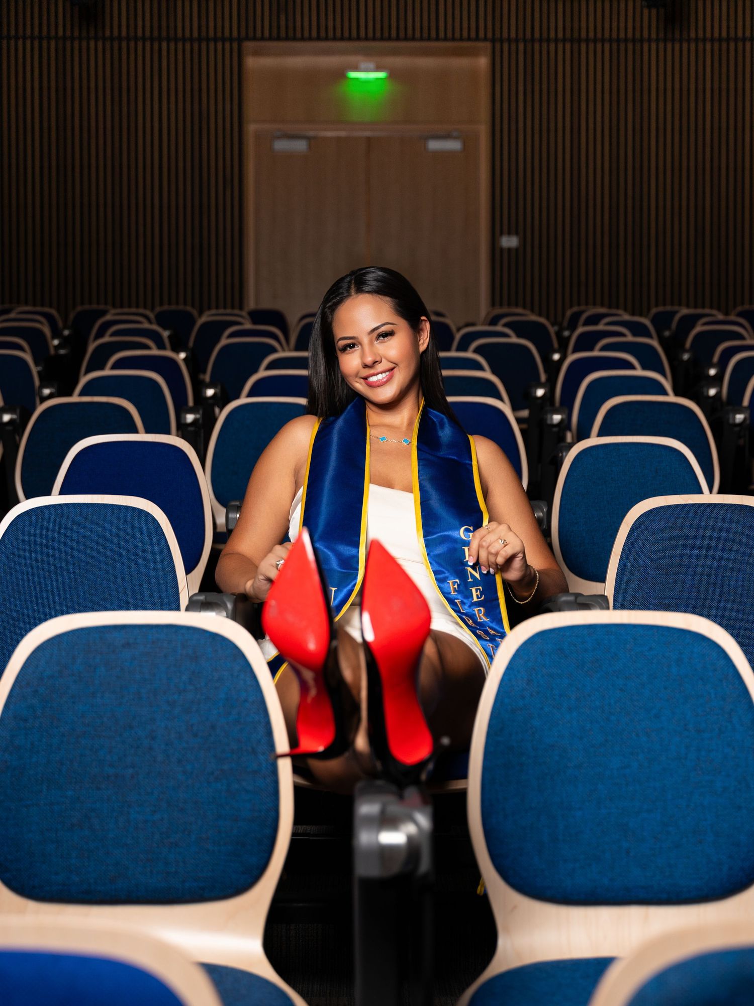 Person in red dress sitting in an empty auditorium with blue seats, creating a striking visual contrast.
