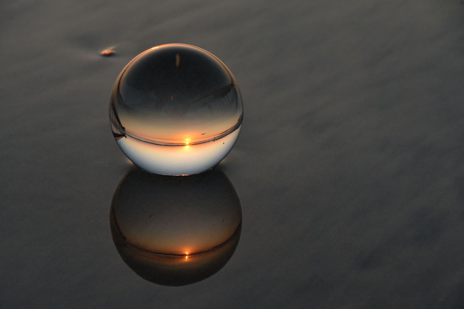 Multiple reflections of a pier and sunset are found in this image of a crystal ball on the beach.