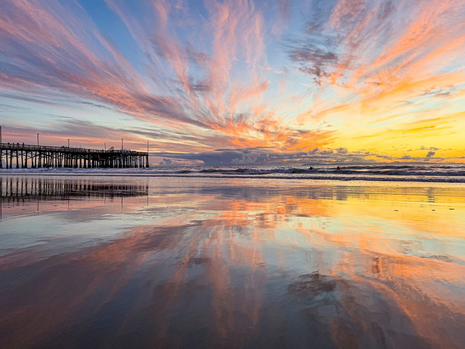 A beautiful sunset and pier at Newport Beach, California is reflected in the wet sand.