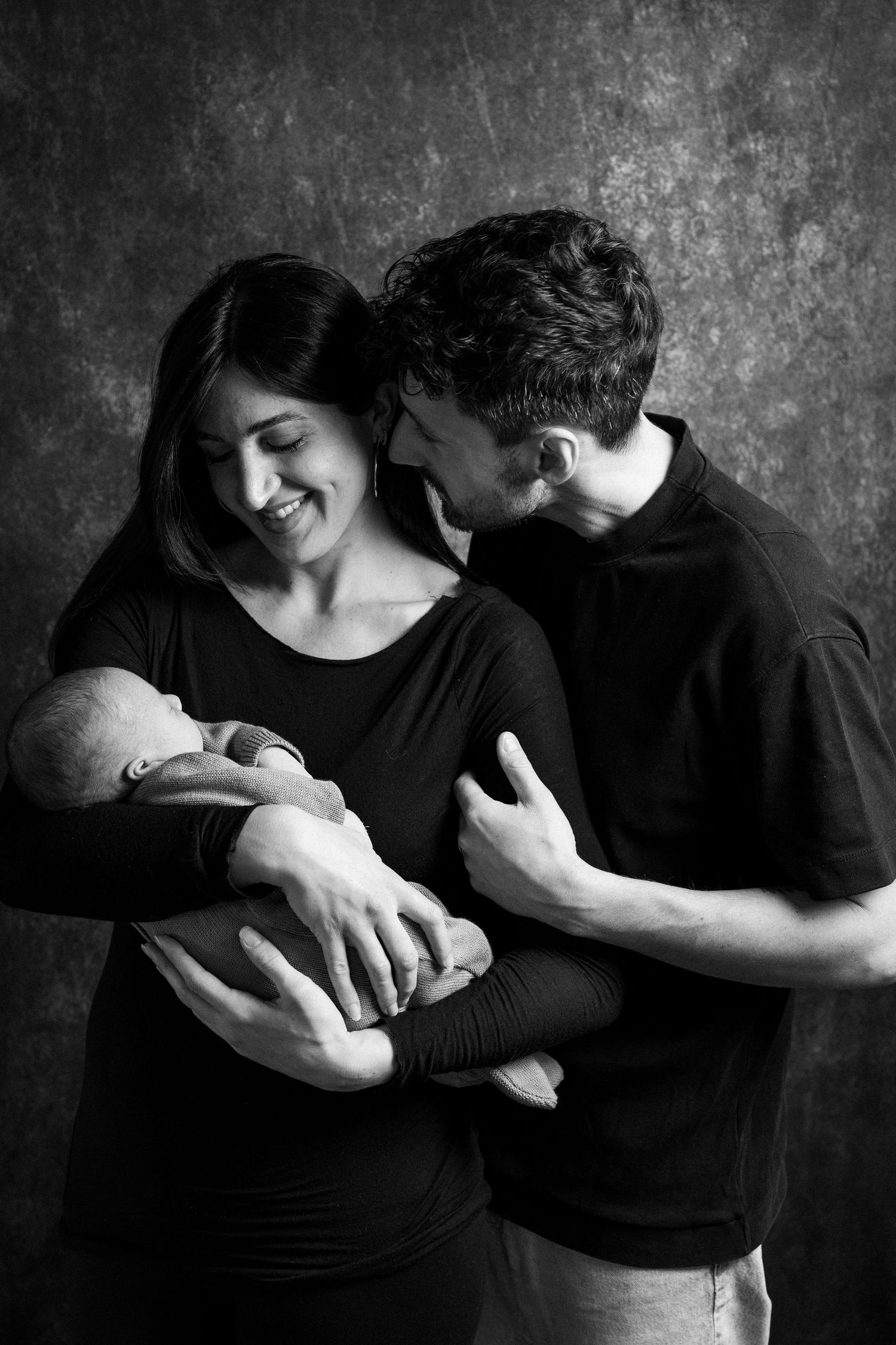 A series of black and white intimate photos showing a couple embracing in tender moments against a dark textured background.