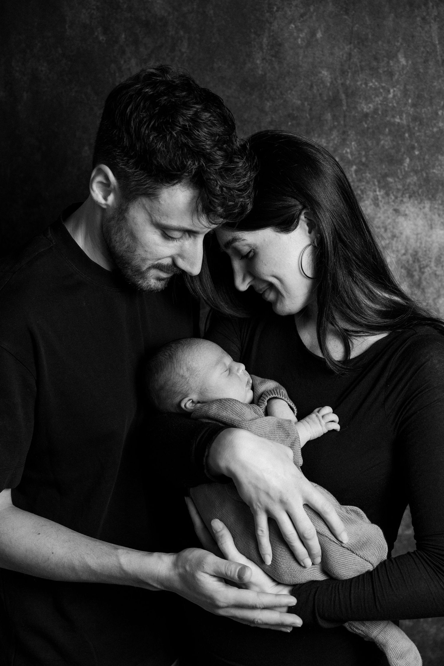 A tender black and white portrait of a couple gazing lovingly at their newborn baby.