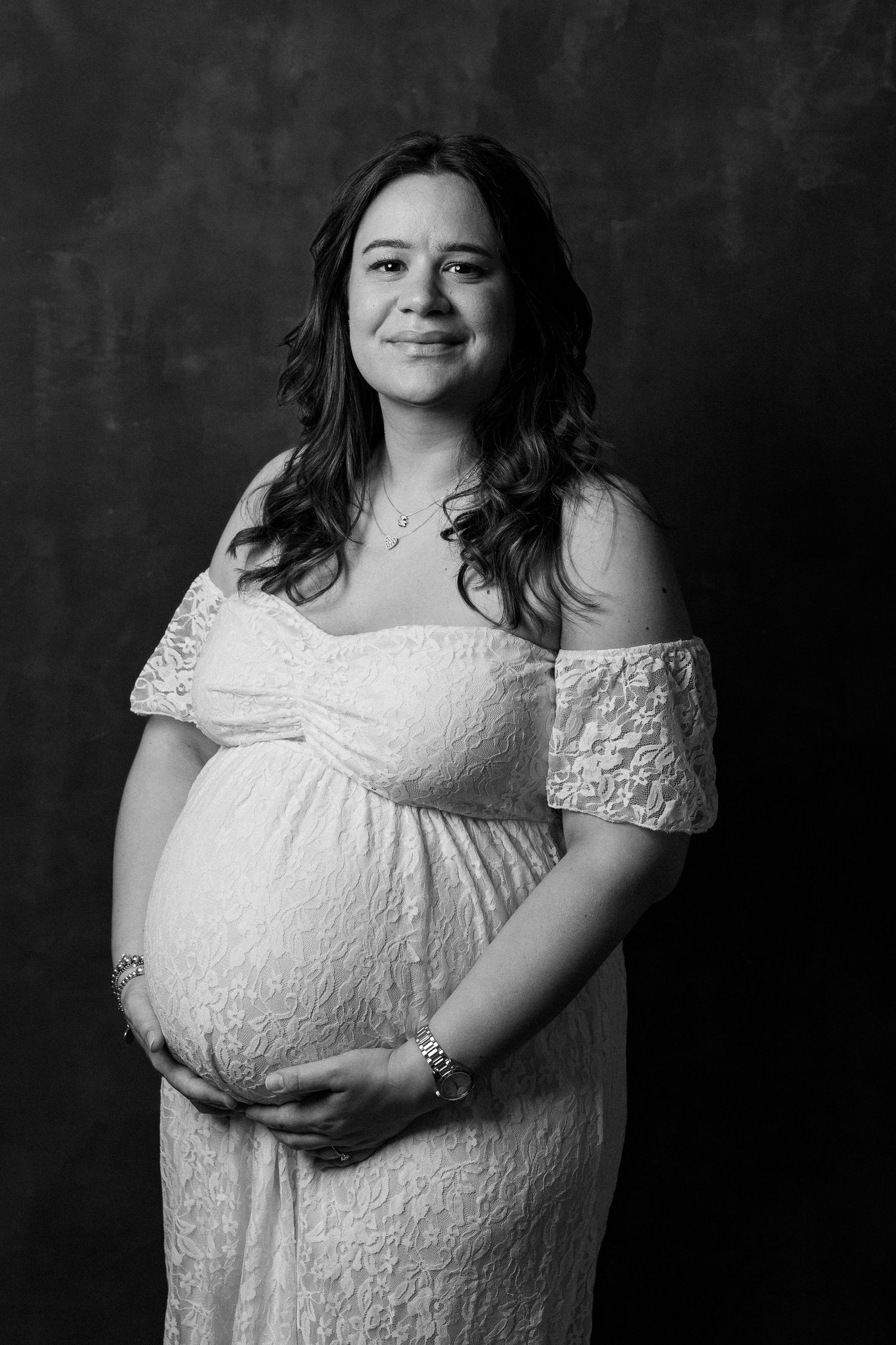 Black and white maternity portrait series showing a pregnant woman in white lace dress from different angles.