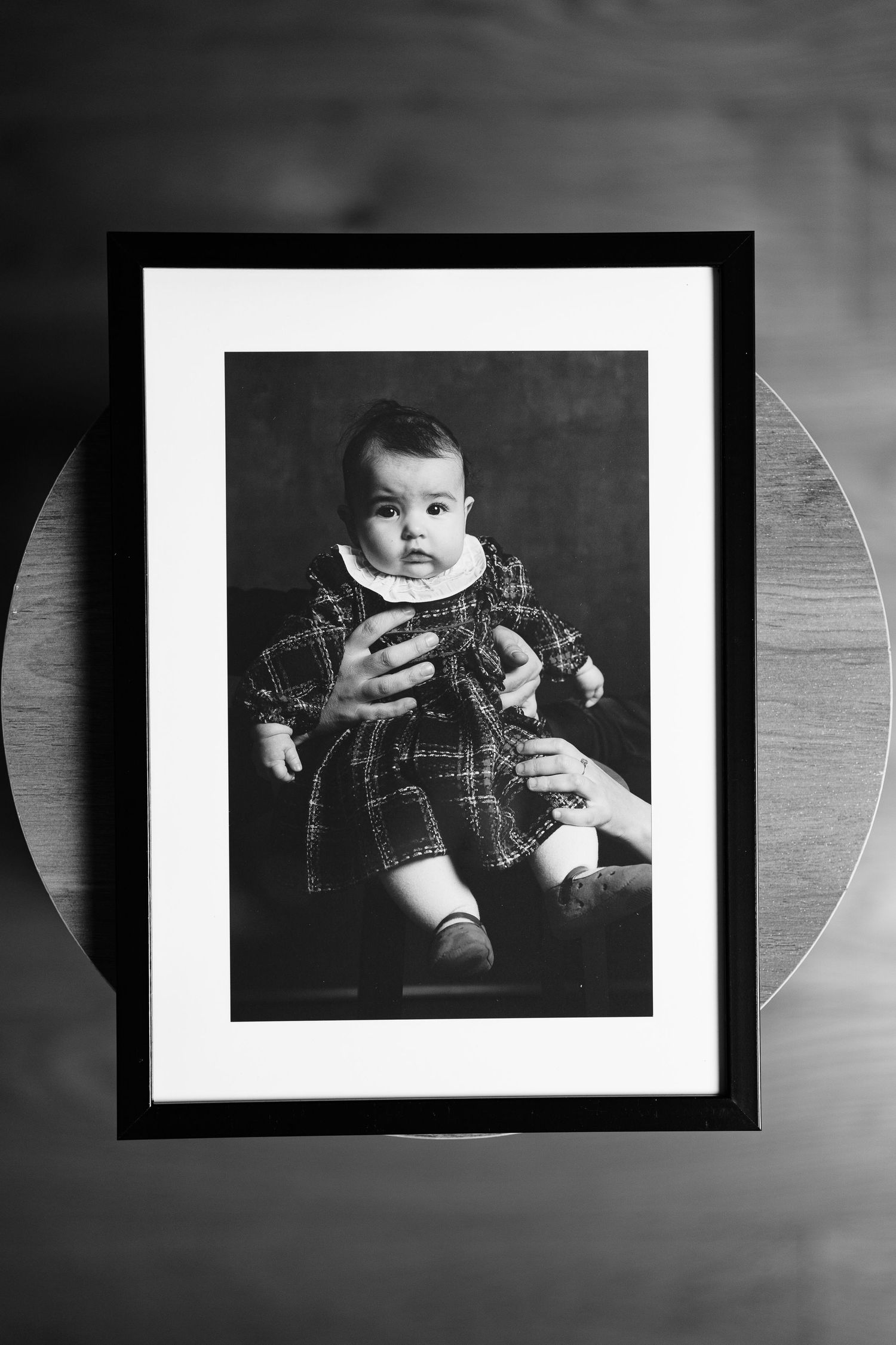 Black and white photo series showing a baby in a plaid shirt displayed in multiple framed portraits against a dark background.