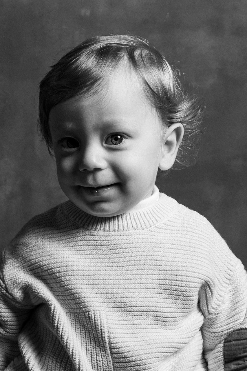 Black and white portrait sequence showing a young child in white sweater with playful expressions.