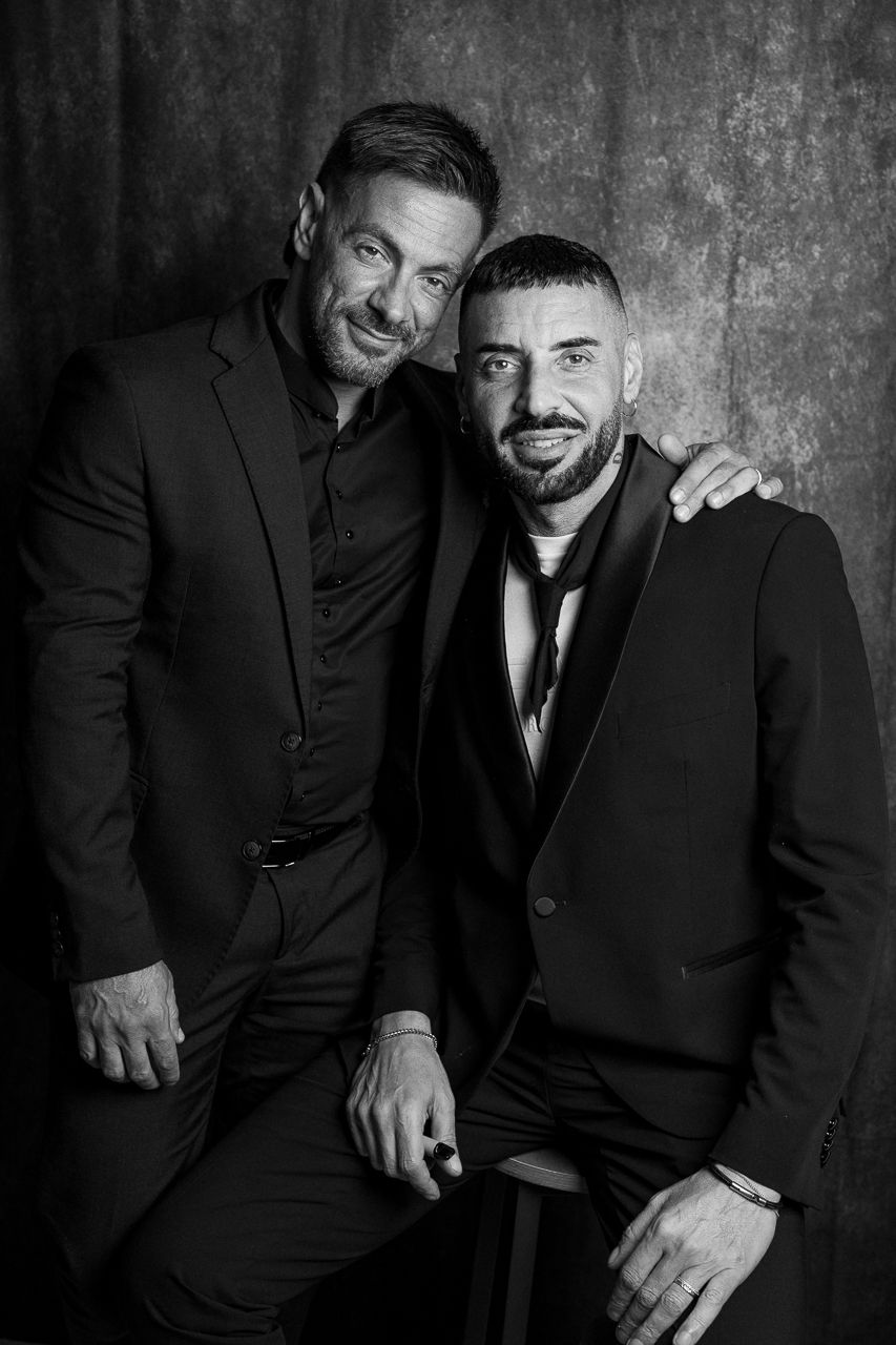 Professional black and white portrait series of two people in suits against textured wall.