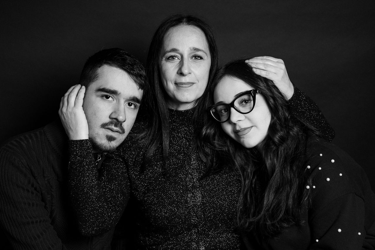 Dark moody family portrait with people wearing black clothing against black background.