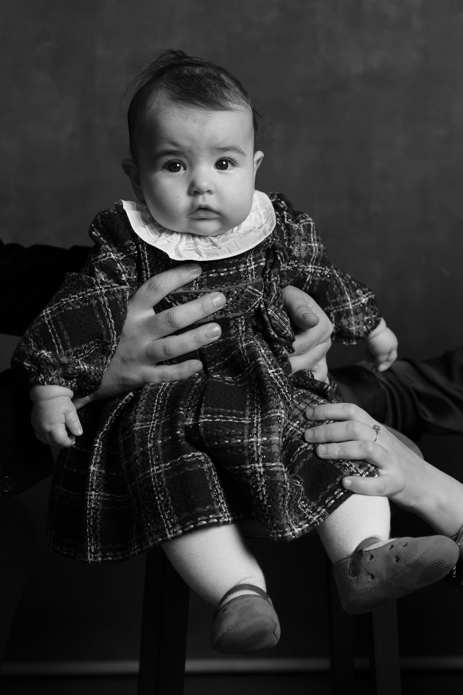 A series of black and white photos showing a baby in a plaid outfit being held and supported by adult hands.