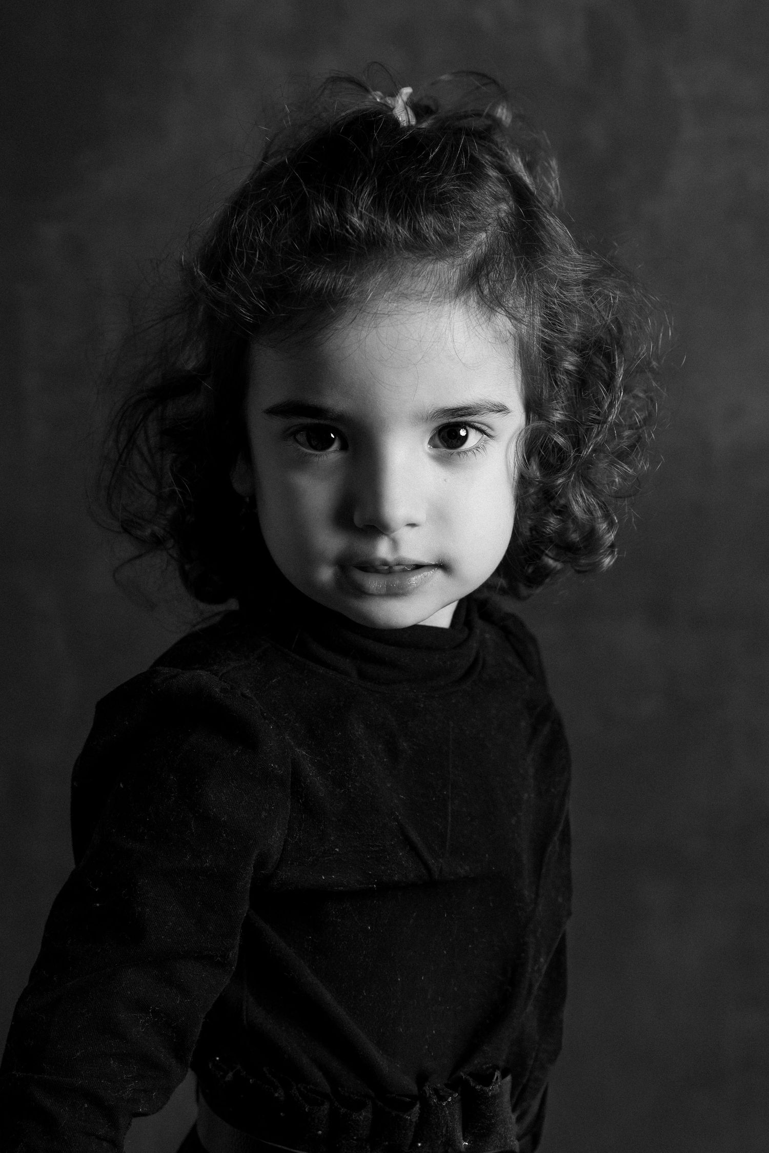 Artistic black and white portrait series of a child in dark clothing with curly hair.