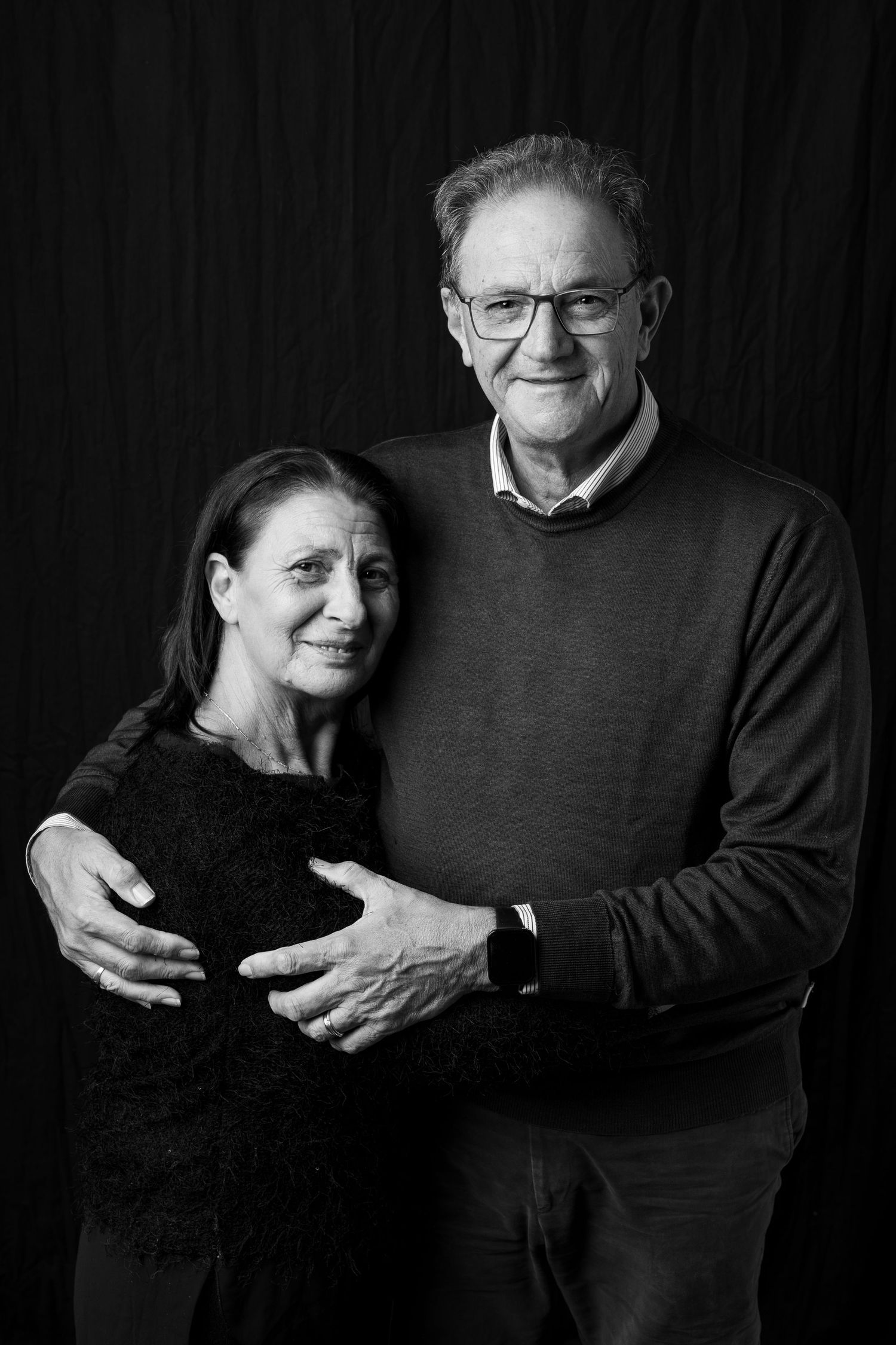 Intimate black and white portrait series showing affectionate embrace against dark backdrop.