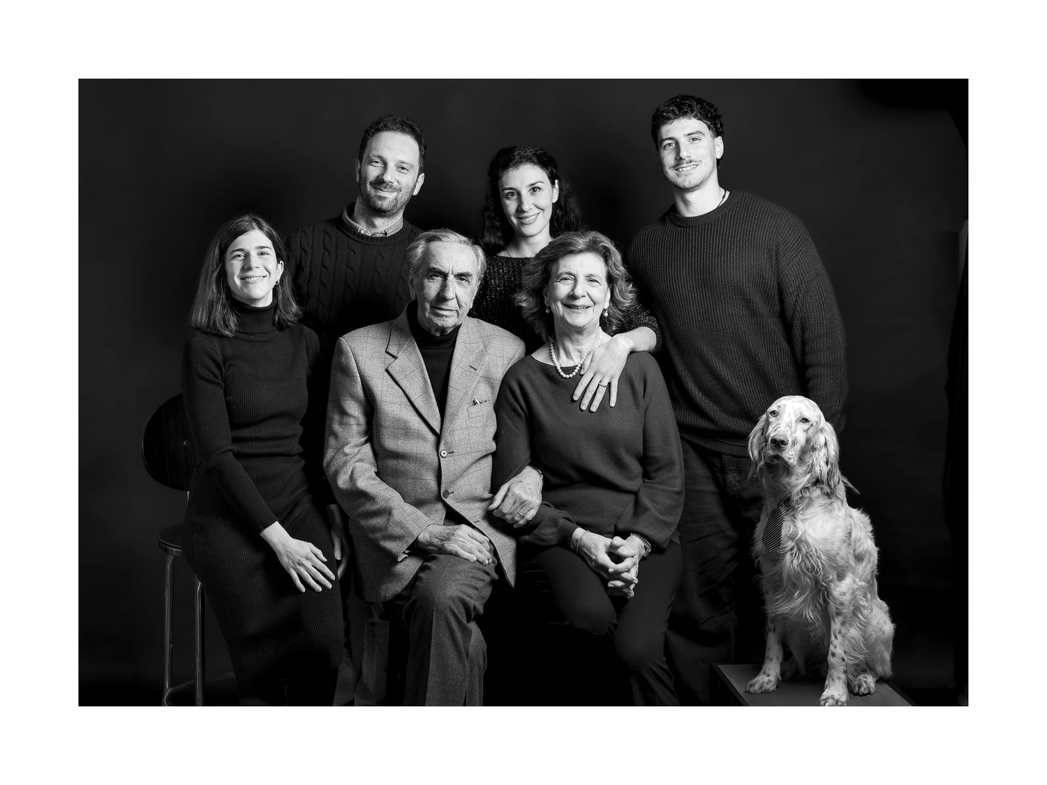 Black and white family portrait series showing loving moments with a dog against dark background.