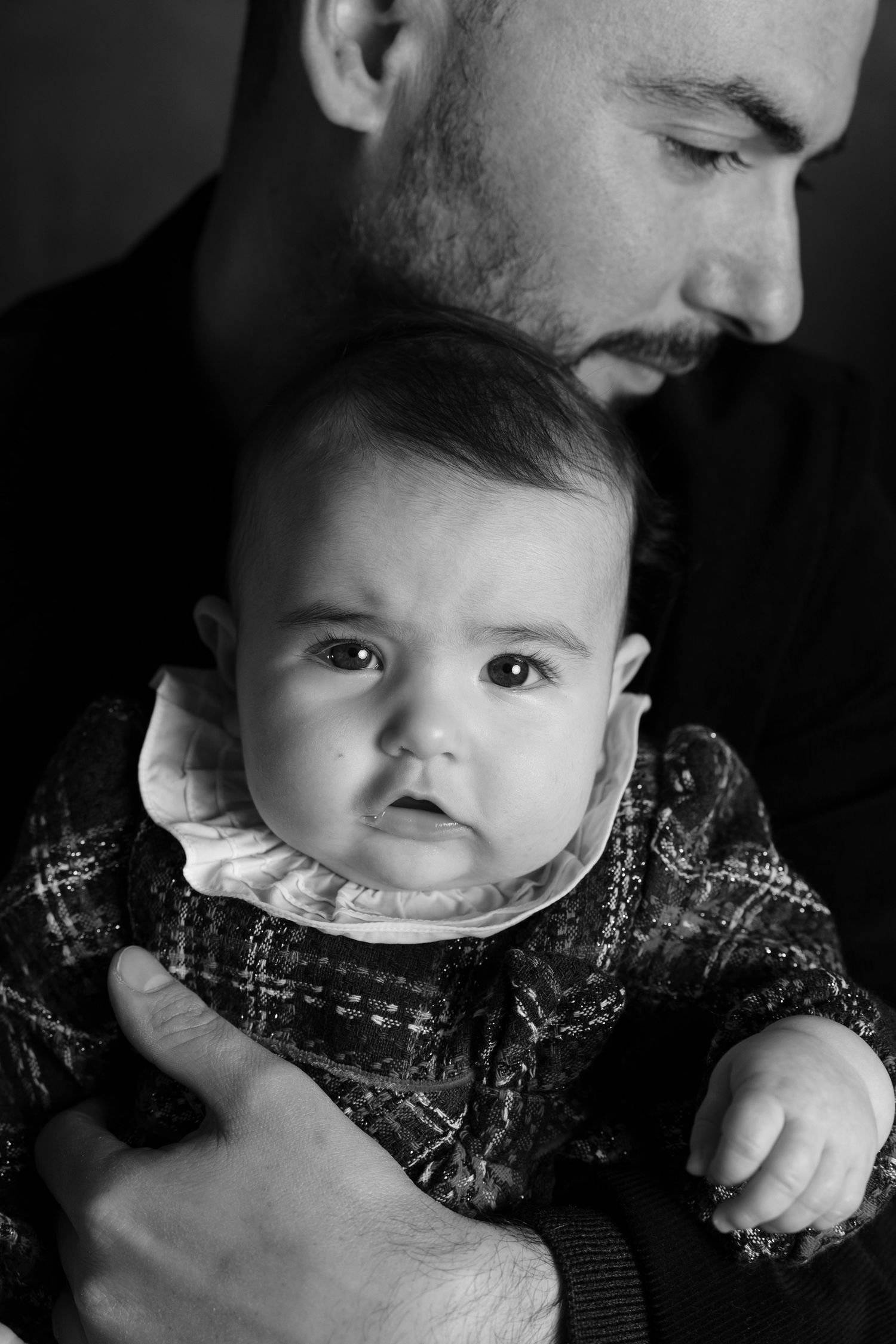 Black and white close-up portrait of an infant being held while wearing plaid clothing.