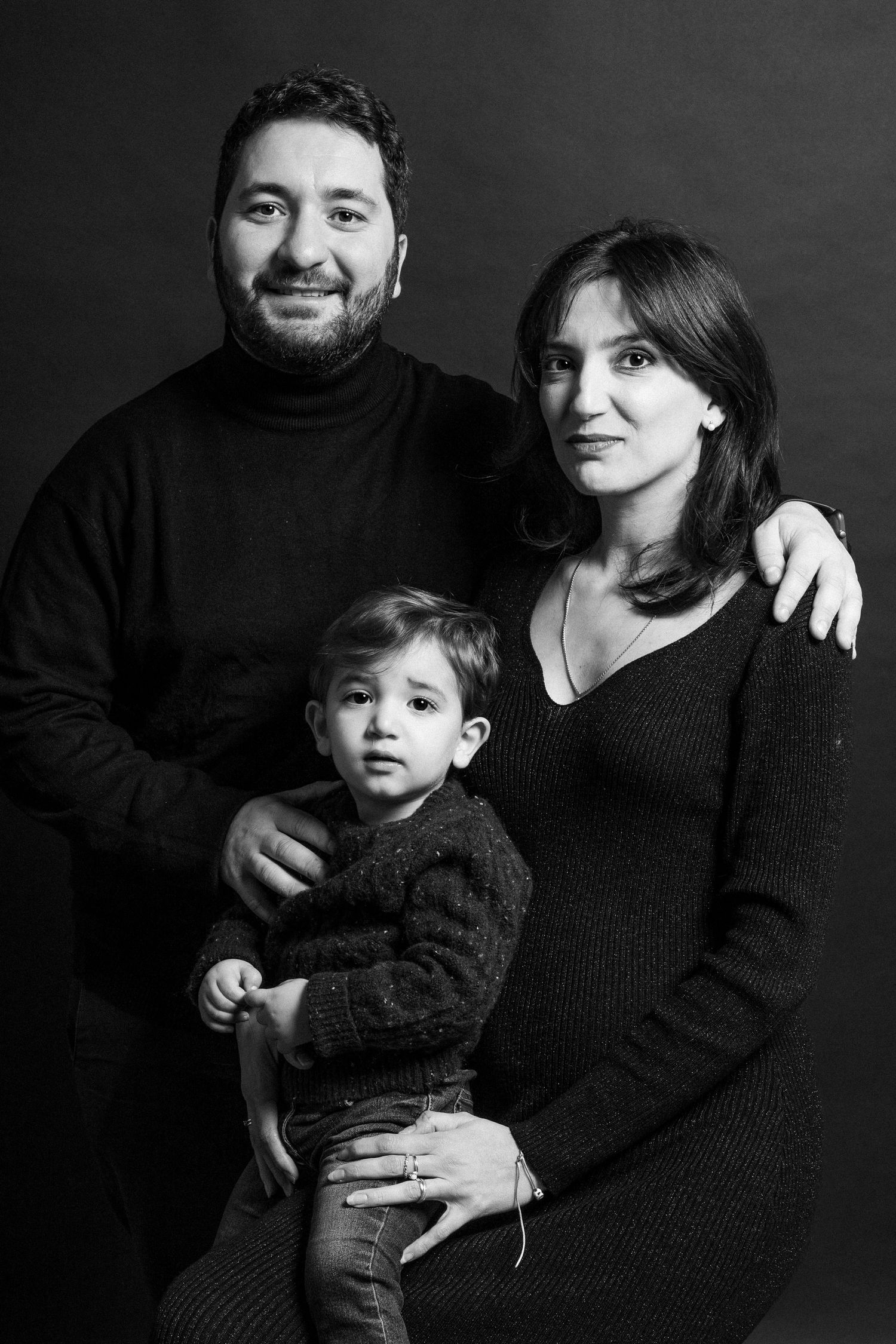 Black and white family portrait series showing intimate moments against dark background.