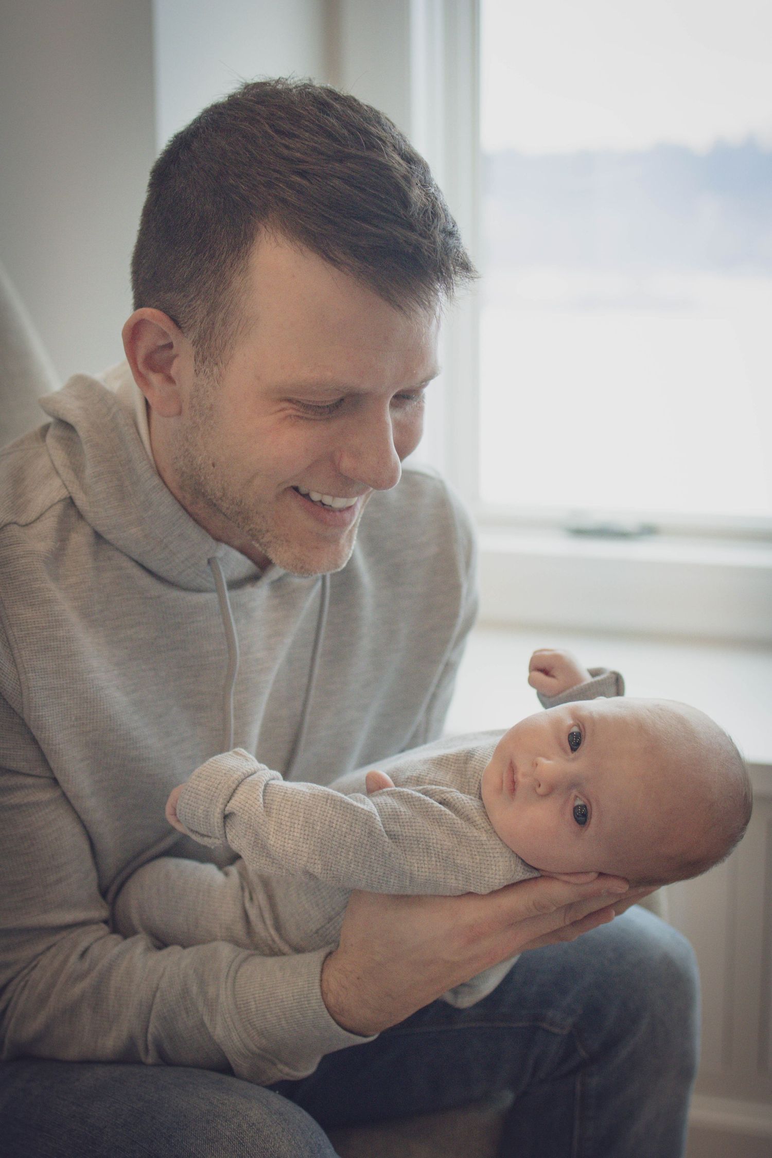 Andover newborn photographer capturing a black‑and‑white lifestyle portrait of a dad holding baby by a window in their home in Andover.
